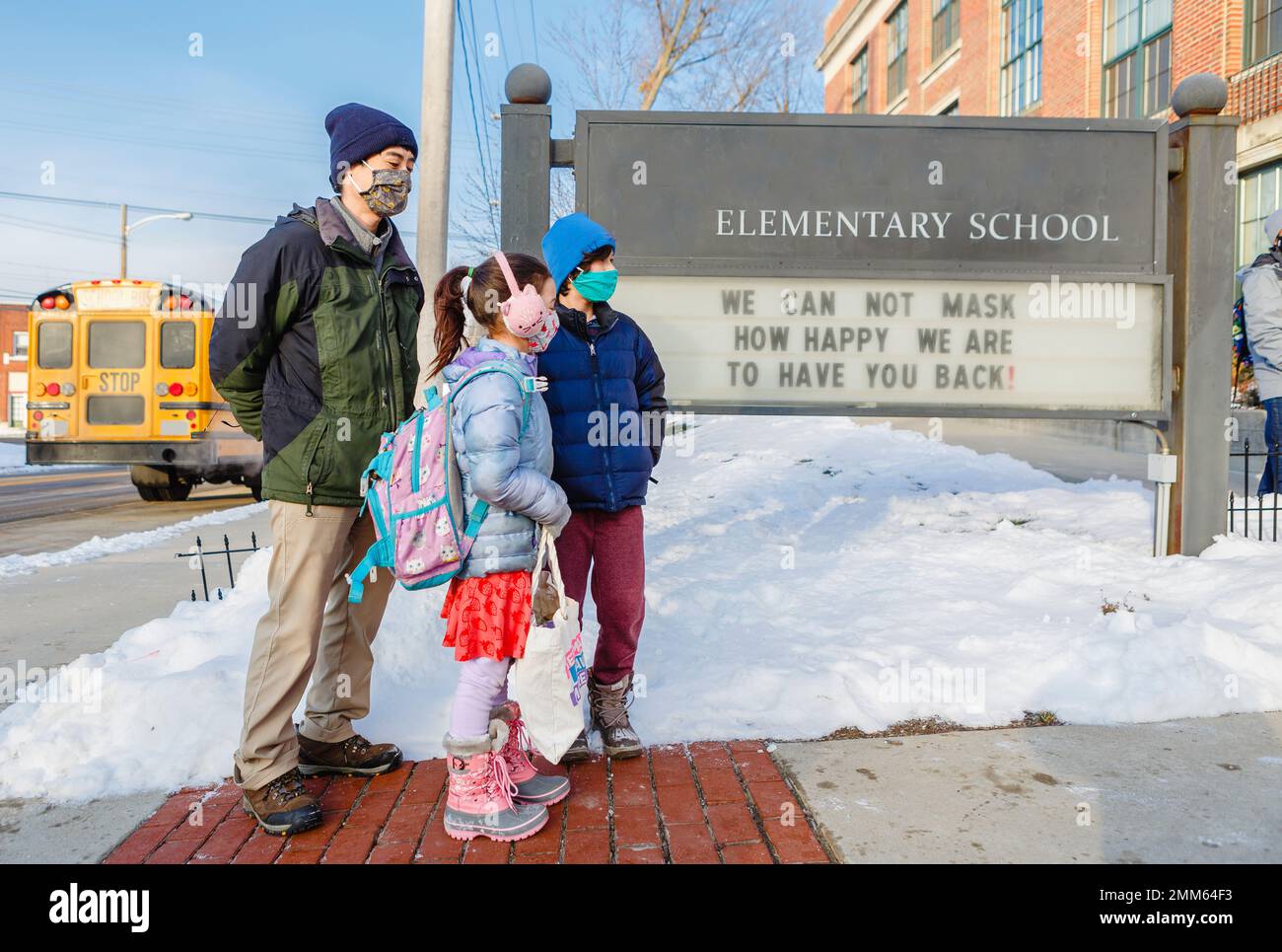 Ein maskierter Vater wartet vor der Grundschule mit zwei Kindern Stockfoto