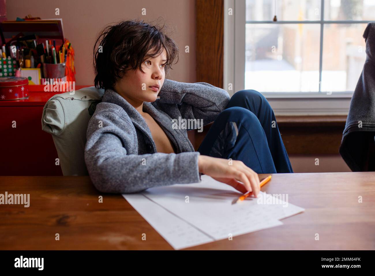 Ein Junge in Cardigan sitzt am Tisch und arbeitet an den Hausaufgaben Stockfoto