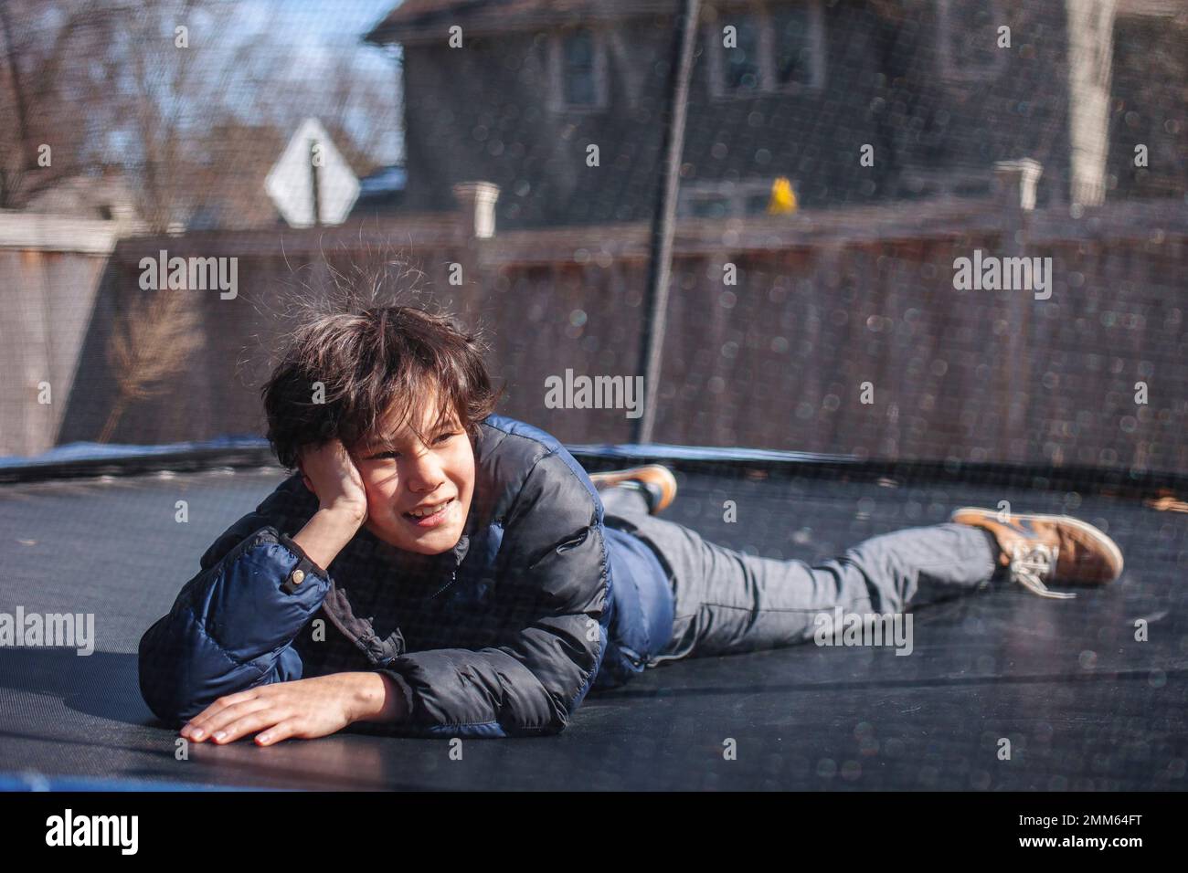 Ein lächelnder Junge liegt im Winter draußen auf einem Trampolin Stockfoto
