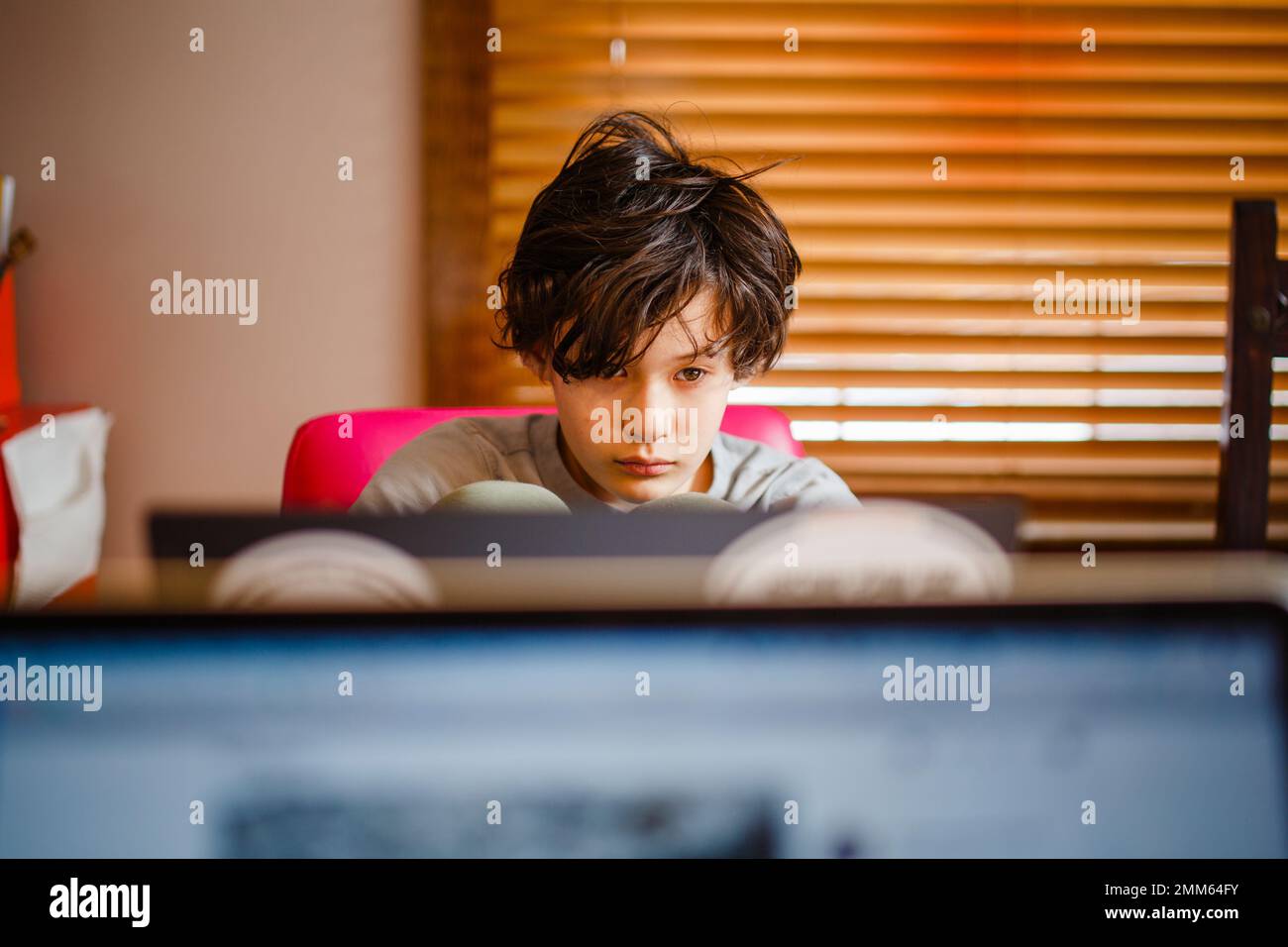 Ein Junge sitzt zu Hause an einem Computer und arbeitet an Schularbeiten Stockfoto