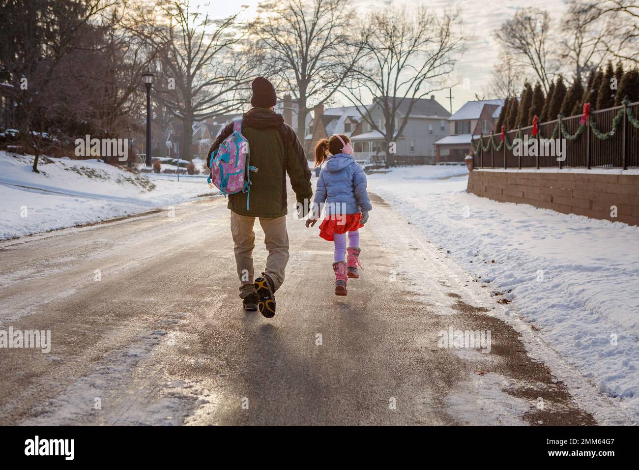 Rückansicht von Vater und Tochter, die auf einer schneebedeckten Straße zur Schule gehen Stockfoto