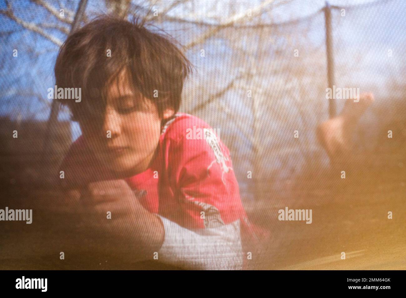 Blick auf den Jungen durch Trampolinnetz im Sonnenlicht Stockfoto
