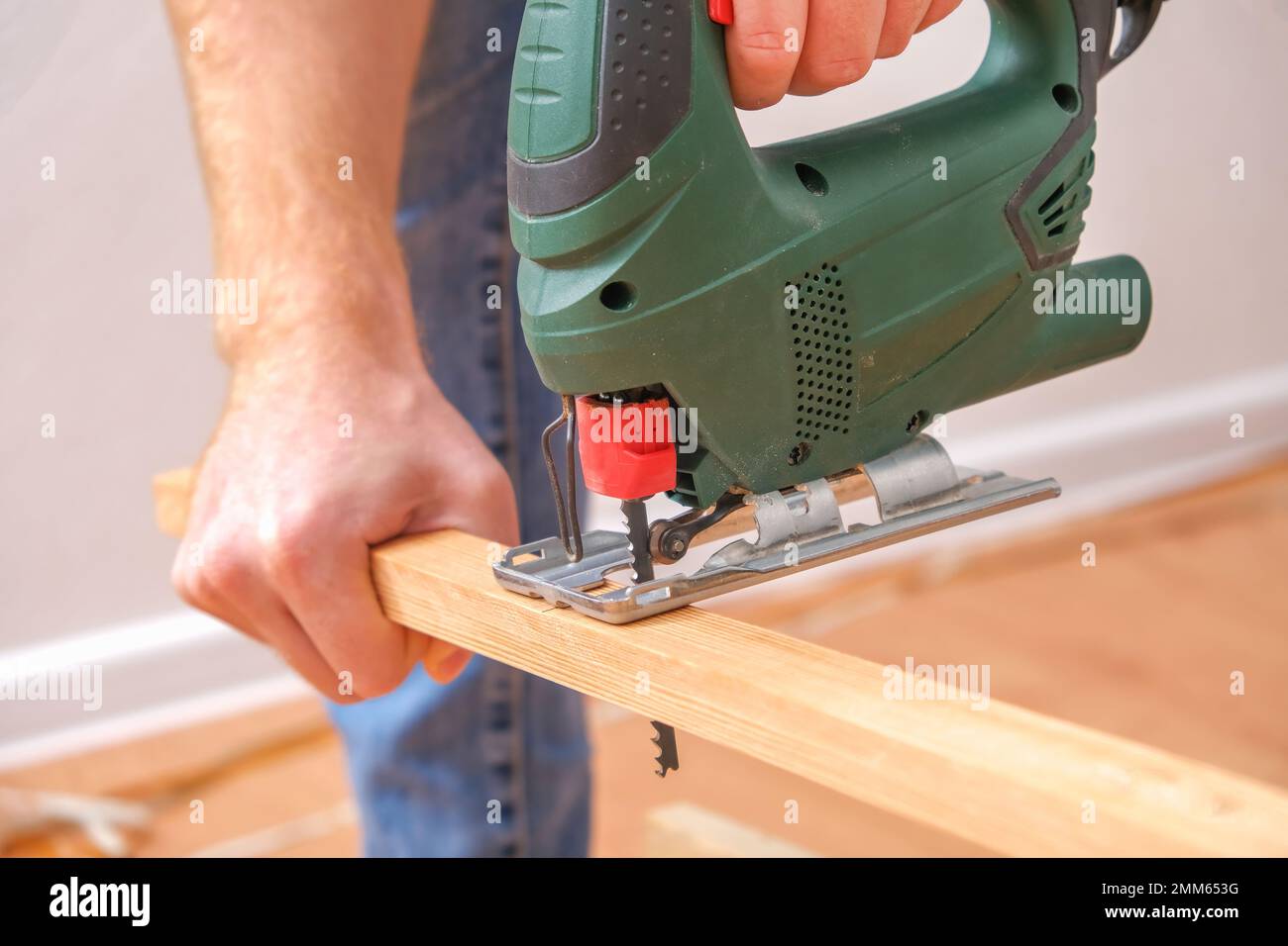 Die Hände eines Zimmermanns mit einer elektrischen Stichsäge in den Händen, die ein Stück Holz abschneidet. Männliche Hände mit Laubsäge zum Schneiden von Holz. Ein Zimmermann schneidet Holz mit einer Stichsäge in einer heimischen Werkstatt. Stockfoto
