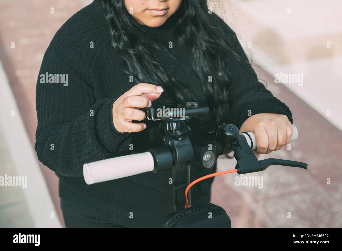 latina-Frau, die einen Elektroroller mit einer Smartphone-Anwendung fährt Stockfoto