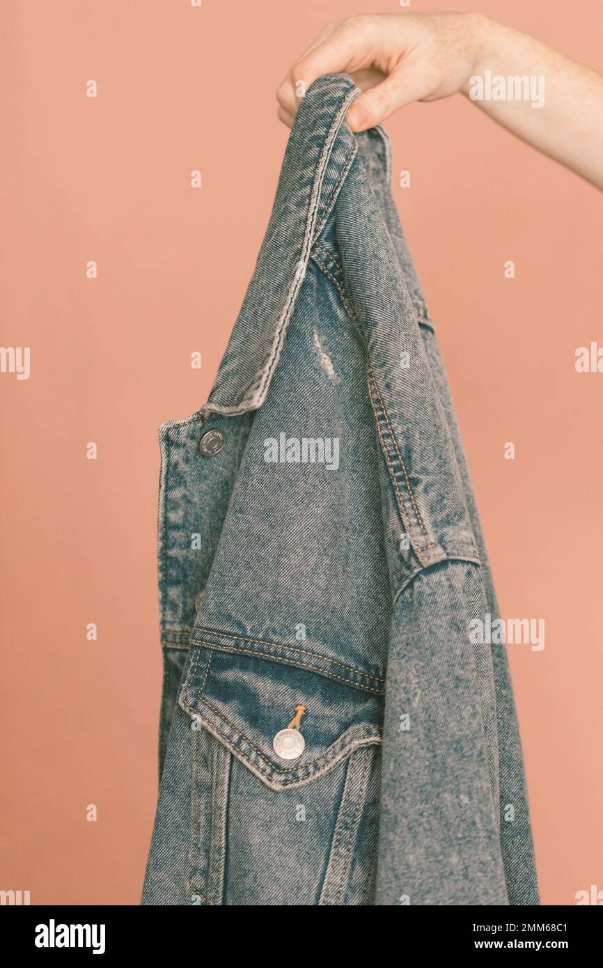 Hand hält eine jeansjacke vor einem pinkfarbenen Hintergrund Stockfoto