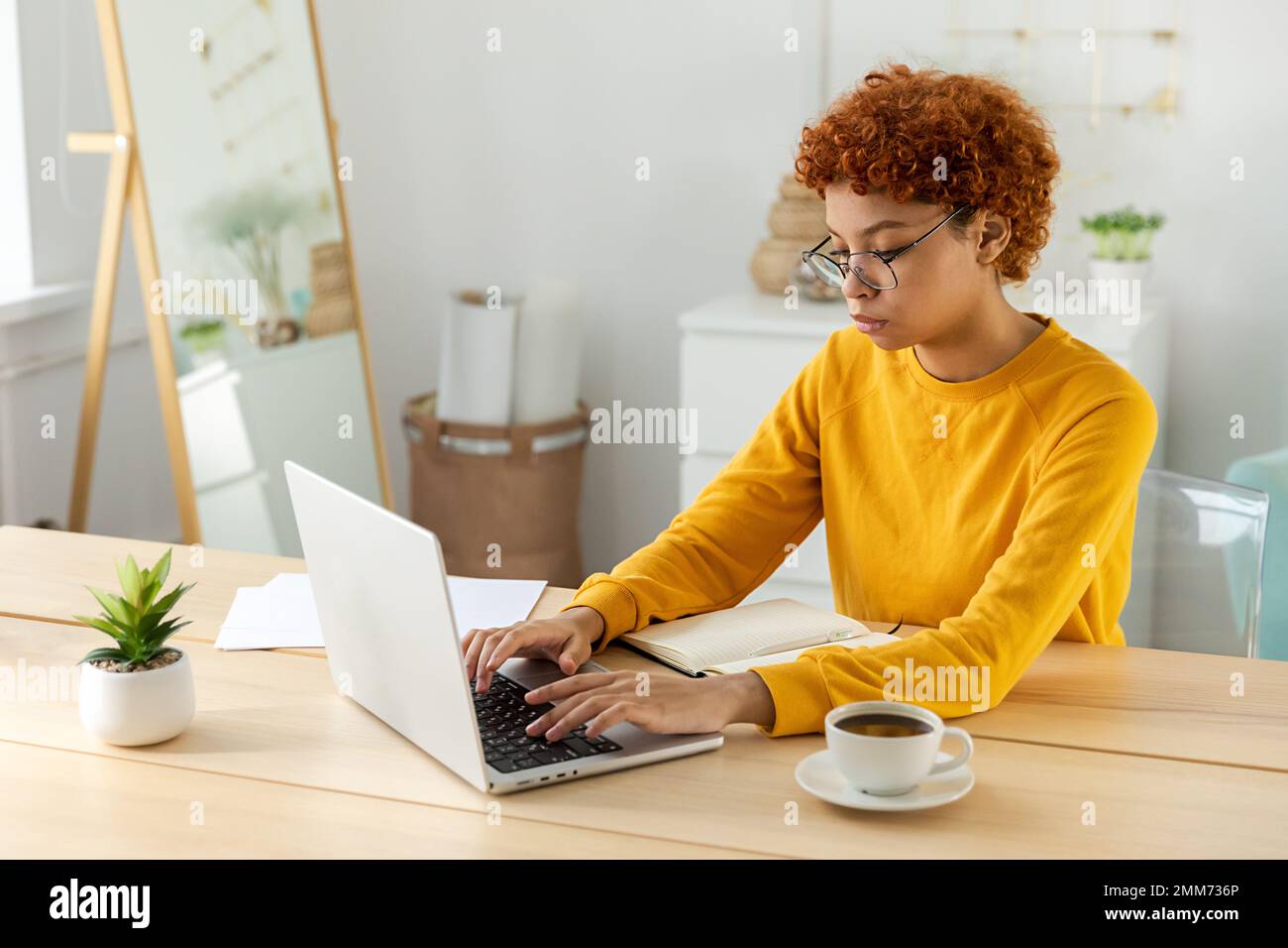 Ein afroamerikanisches Mädchen, das ein Notebook im Heimbüro benutzt, auf dem Bildschirm tippt, chattet und E-Mails schreibt. Junge Frau, die ein virtuelles Meeting hat, Online-Chat, Videokonferenz. Arbeit Lernen von zu Hause Stockfoto