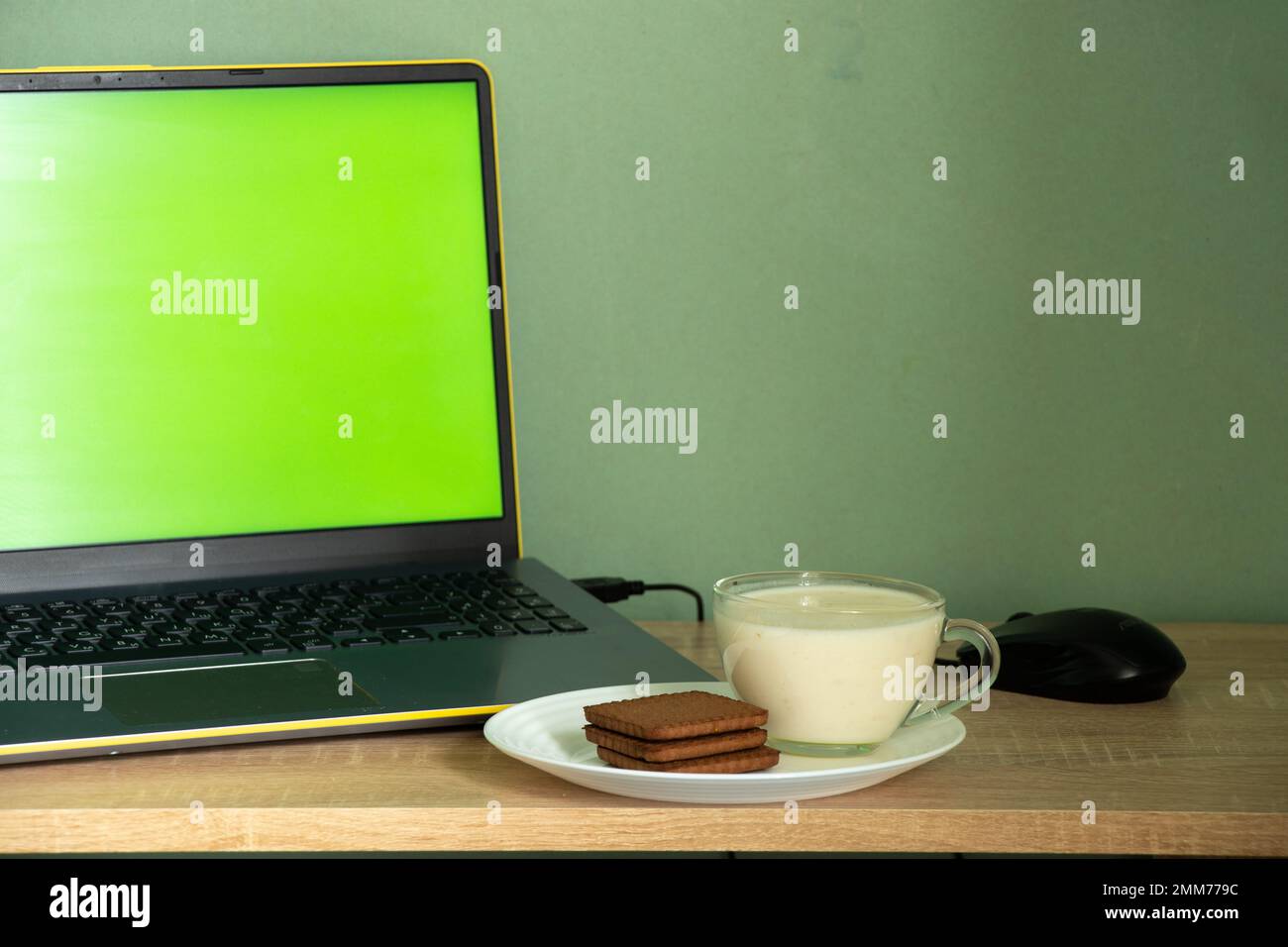 Laptop mit grünem Bildschirm-Joghurt mit Keksen auf einem Tisch in einem Zimmer zu Hause Stockfoto