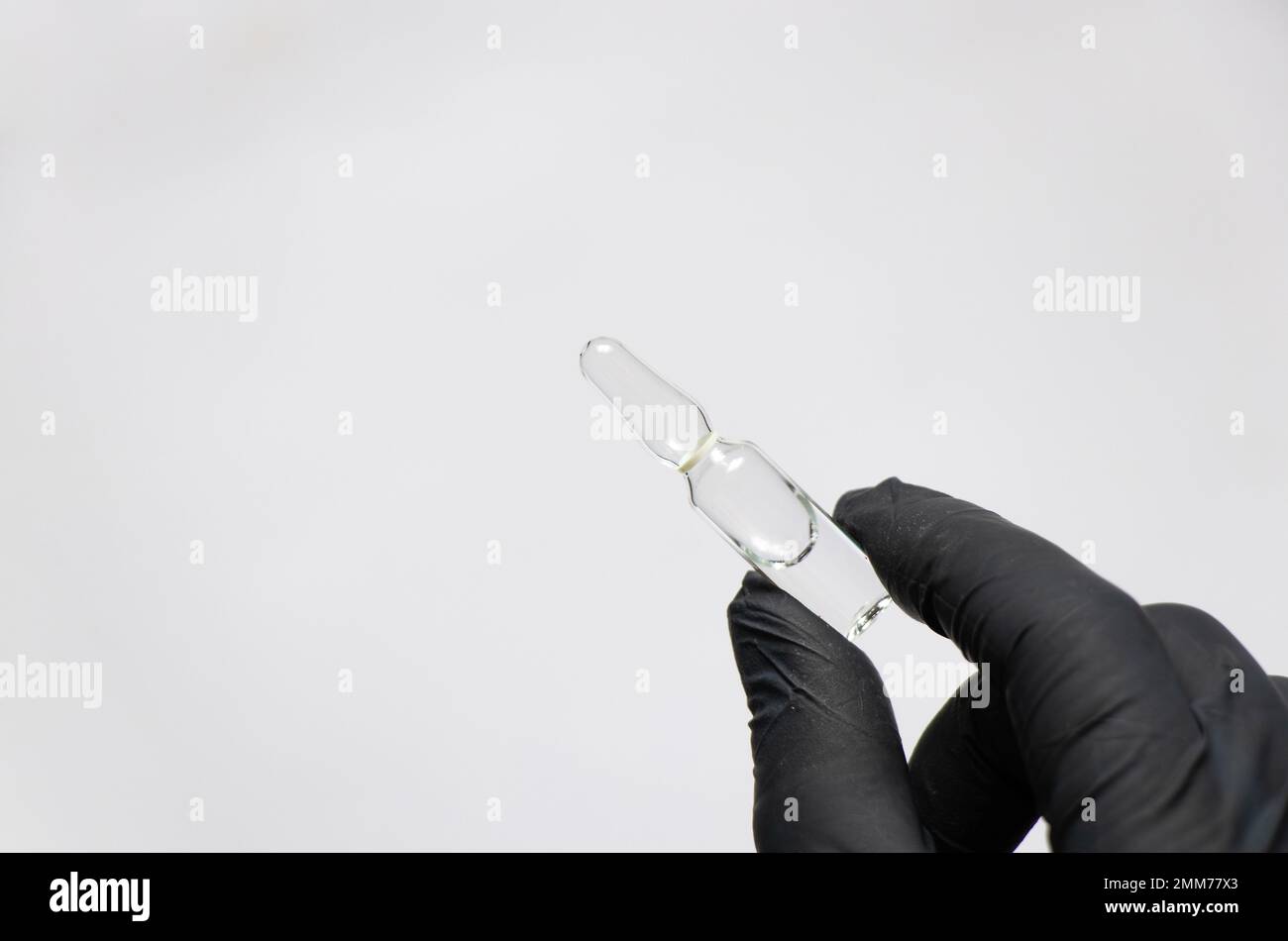 Die Hand in schwarzen Handschuhen hält eine Ampulle mit dem Medikament Stockfoto