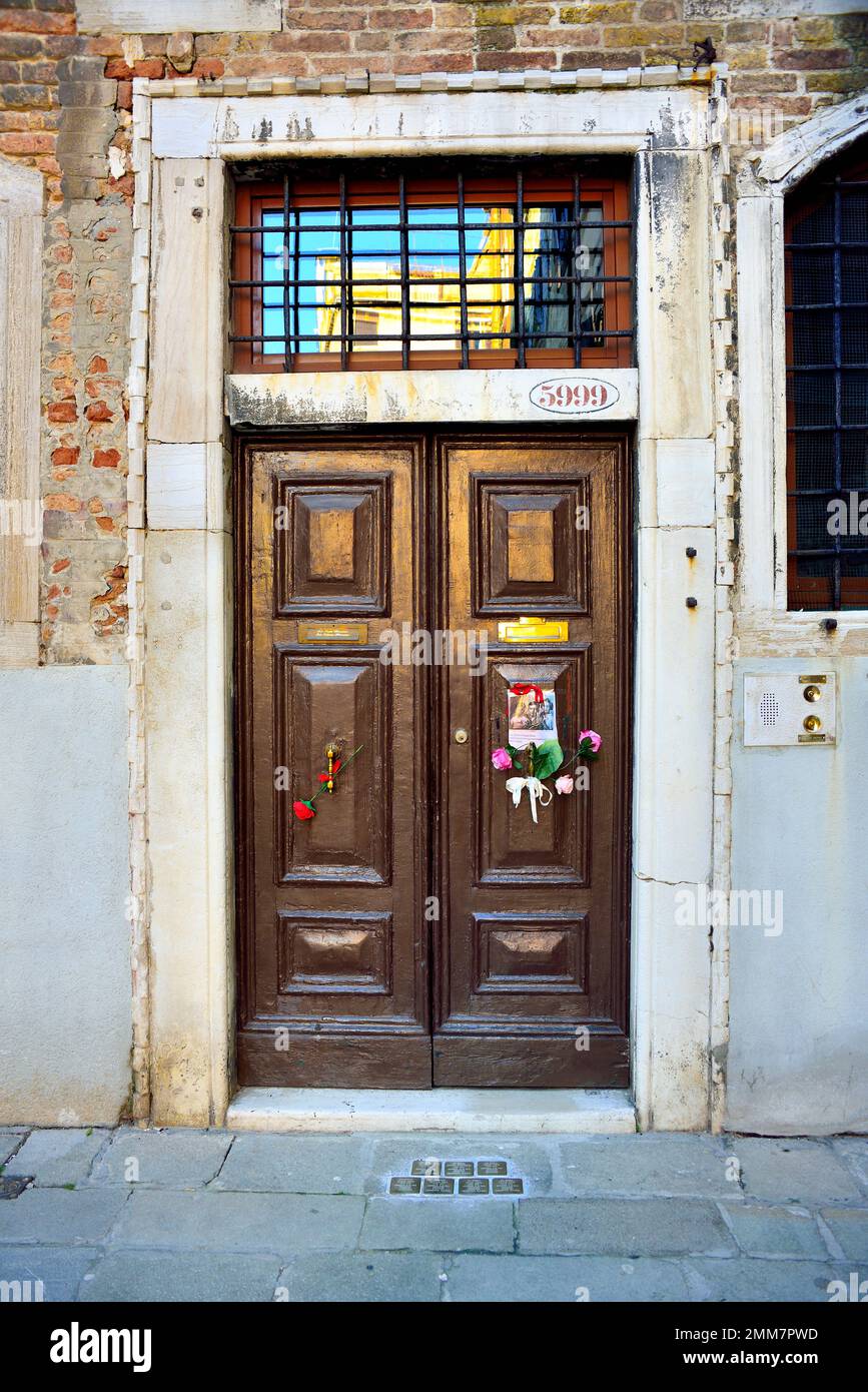 Am Holocaust-Gedenktag 2023 steckte eine anonyme Hand das Bild von drei Kindern und ein paar Blumen an die alte Tür, Nummer 5999 Cannaregio, in Venedig. Die Kinder wurden 1943 mit ihren Eltern und ihrem einjährigen Bruder nach Auschwitz deportiert. Sie waren 14, 10, 7 Jahre alt. Sie wurden am 26. Februar 1944 in Auschwitz mit ihrem einjährigen Bruder getötet. Vor einigen Jahren wurden 7 „Steine“ am Eingang ihres Hauses platziert. Auf dem Foto steht: " Anna, Guido und Giorgia Dina. Leone war ein Jahr alt und wir werden nie wissen, welches Gesicht er hatte. Stockfoto