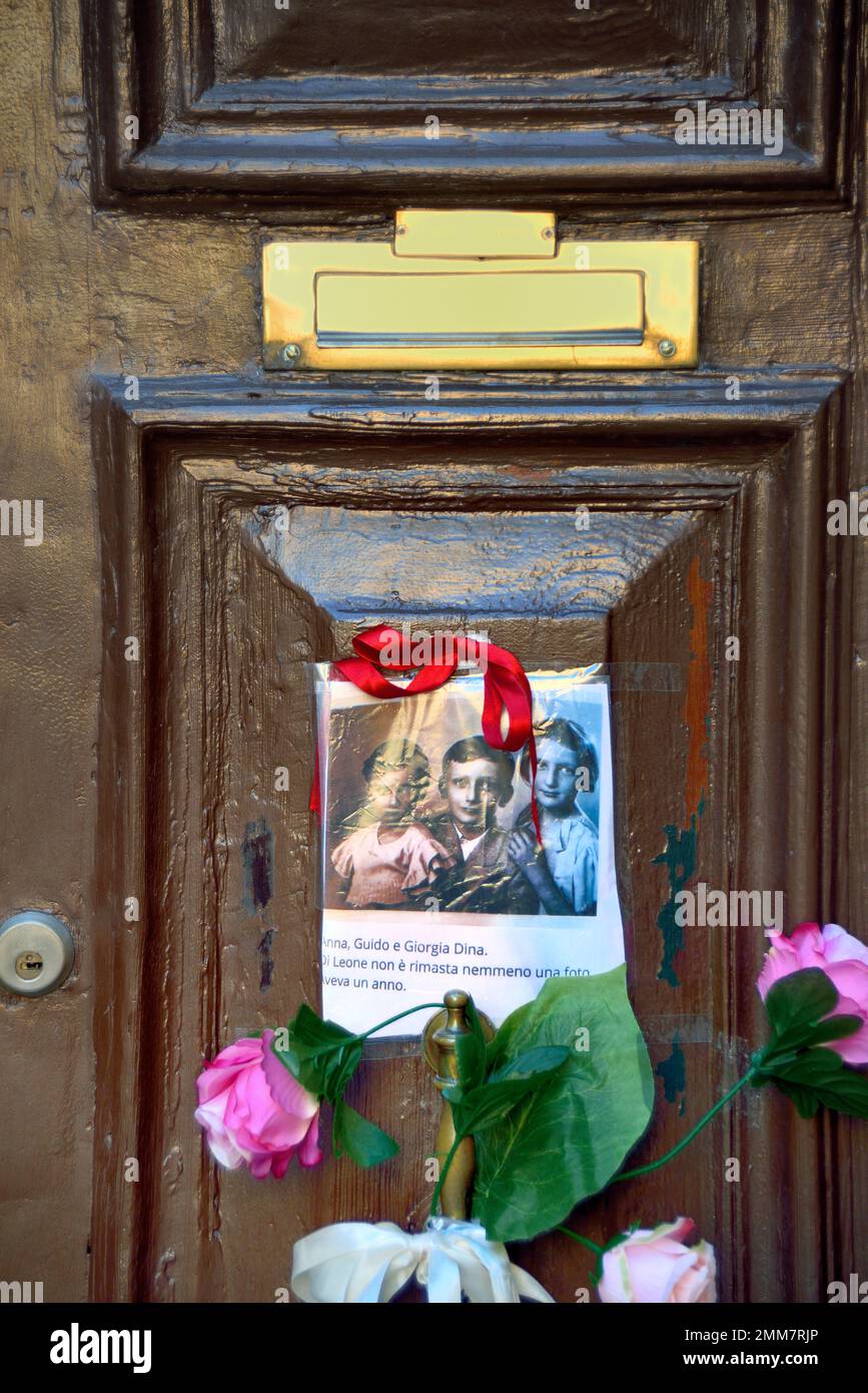 Am Holocaust-Gedenktag 2023 steckte eine anonyme Hand das Bild von drei Kindern und ein paar Blumen an die alte Tür, Nummer 5999 Cannaregio, in Venedig. Die Kinder wurden 1943 mit ihren Eltern und ihrem einjährigen Bruder nach Auschwitz deportiert. Sie waren 14, 10, 7 Jahre alt. Sie wurden am 26. Februar 1944 in Auschwitz mit ihrem einjährigen Bruder getötet. Vor einigen Jahren wurden 7 „Steine“ am Eingang ihres Hauses platziert. Auf dem Foto steht: " Anna, Guido und Giorgia Dina. Leone war ein Jahr alt und wir werden nie wissen, welches Gesicht er hatte. Stockfoto