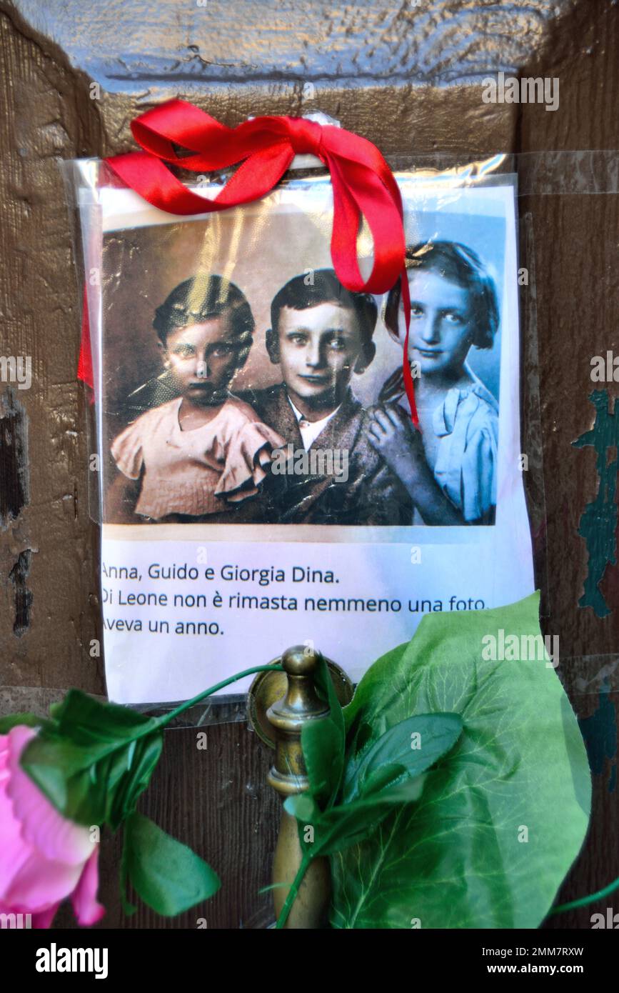 Am Holocaust-Gedenktag 2023 steckte eine anonyme Hand das Bild von drei Kindern und ein paar Blumen an die alte Tür, Nummer 5999 Cannaregio, in Venedig. Die Kinder wurden 1943 mit ihren Eltern und ihrem einjährigen Bruder nach Auschwitz deportiert. Sie waren 14, 10, 7 Jahre alt. Sie wurden am 26. Februar 1944 in Auschwitz mit ihrem einjährigen Bruder getötet. Vor einigen Jahren wurden 7 „Steine“ am Eingang ihres Hauses platziert. Auf dem Foto steht: " Anna, Guido und Giorgia Dina. Leone war ein Jahr alt und wir werden nie wissen, welches Gesicht er hatte. Stockfoto