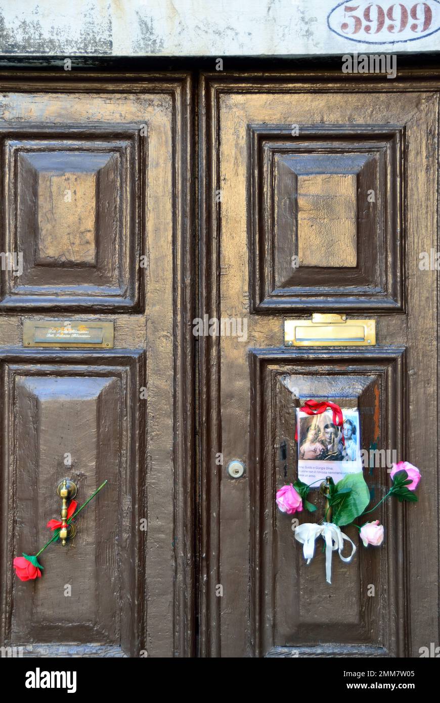 Am Holocaust-Gedenktag 2023 steckte eine anonyme Hand das Bild von drei Kindern und ein paar Blumen an die alte Tür, Nummer 5999 Cannaregio, in Venedig. Die Kinder wurden 1943 mit ihren Eltern und ihrem einjährigen Bruder nach Auschwitz deportiert. Sie waren 14, 10, 7 Jahre alt. Sie wurden am 26. Februar 1944 in Auschwitz mit ihrem einjährigen Bruder getötet. Vor einigen Jahren wurden 7 „Steine“ am Eingang ihres Hauses platziert. Auf dem Foto steht: " Anna, Guido und Giorgia Dina. Leone war ein Jahr alt und wir werden nie wissen, welches Gesicht er hatte. Stockfoto