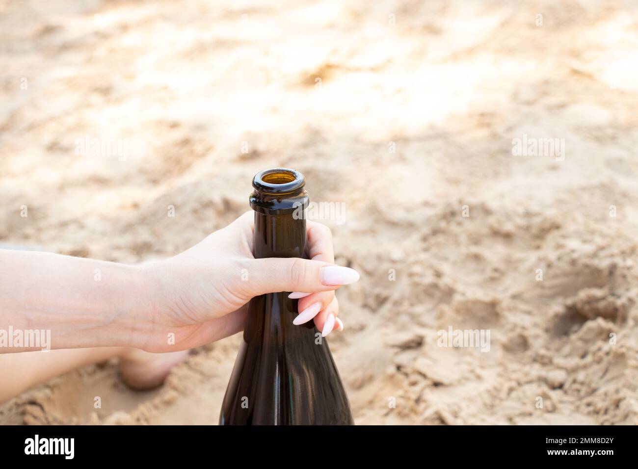 Eine weibliche Hand hält im Sommer am Strand im Urlaub eine Flasche Sekt, eine Flasche Champagner Stockfoto