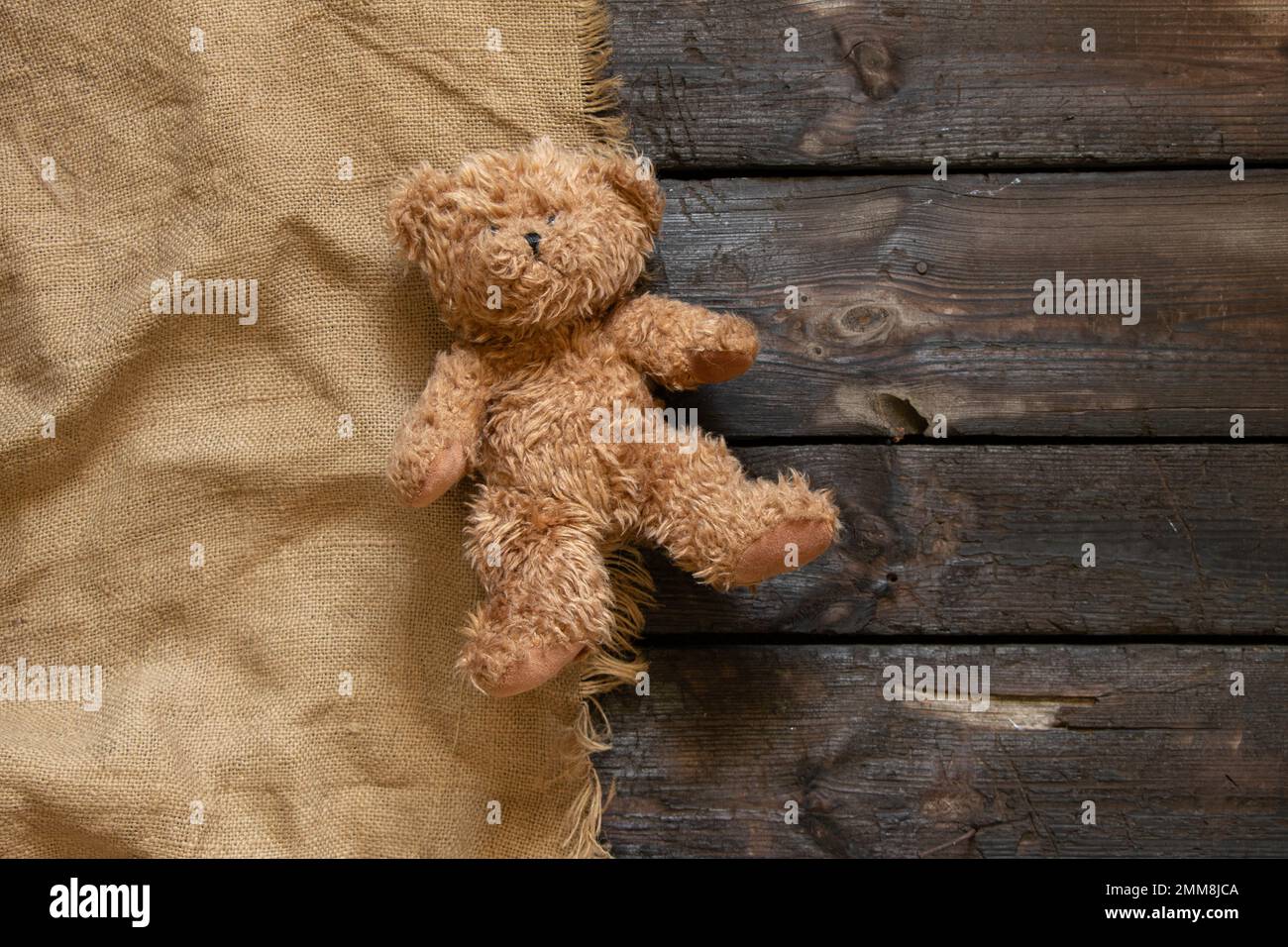 Ein alter brauner Teddybär liegt allein auf einem verkohlten Holzboden auf einem braunen Tuch, ein Kinderspielzeug auf dem Boden Stockfoto