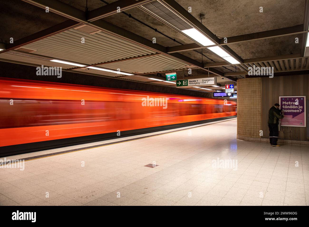 Unscharfe Bewegung des orangefarbenen Zuges, der die U-Bahn-Station Rautatientori in Helsinki, Finnland, verlässt Stockfoto