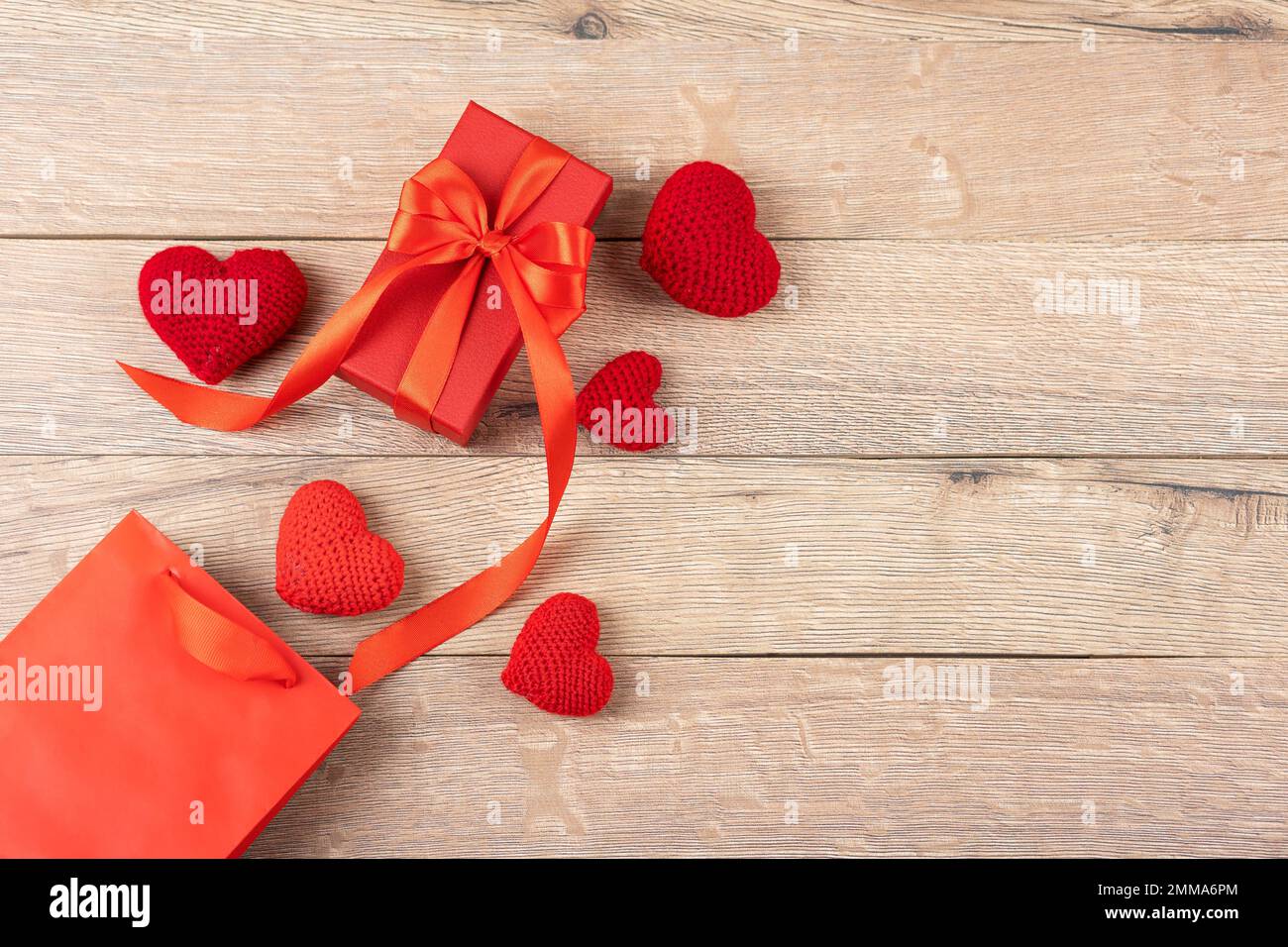 Rote gestrickte Herzen, Geschenkbox und Geschenkpaket auf Holzhintergrund. Grußkarte zum Valentinstag, Muttertag und Geburtstag. Flach verlegt Stockfoto