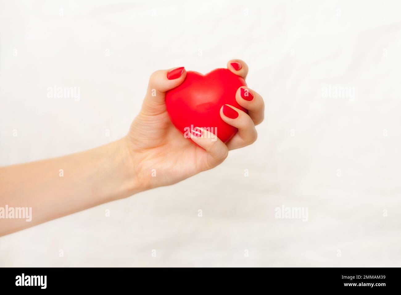 Frauenhand mit roter Maniküre, die rotes Herz auf weiß hält. Krankenschwestern pflegen Herz. Gute Gesundheitsförderung Stockfoto