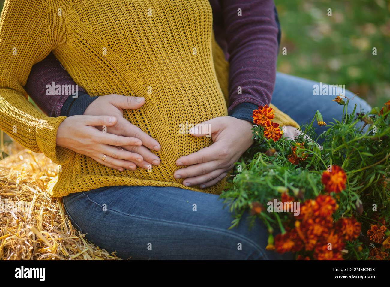 Ein Mann umarmt den Bauch einer schwangeren Frau. Schwangerschaft, Liebe, Familie und Menschen Konzept - Nahaufnahme einer schwangeren Frau, die eine Hand-Herz-Geste auf dem Bauch macht. Stockfoto