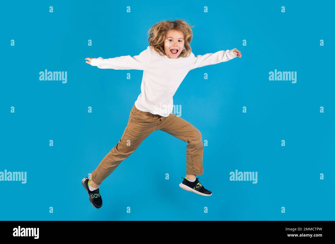 Durchgehende Körpergröße des sorgenfreien Kindersprungs isoliert auf blauem Hintergrund. Ein Junge springt und hebt die Hand. Stockfoto