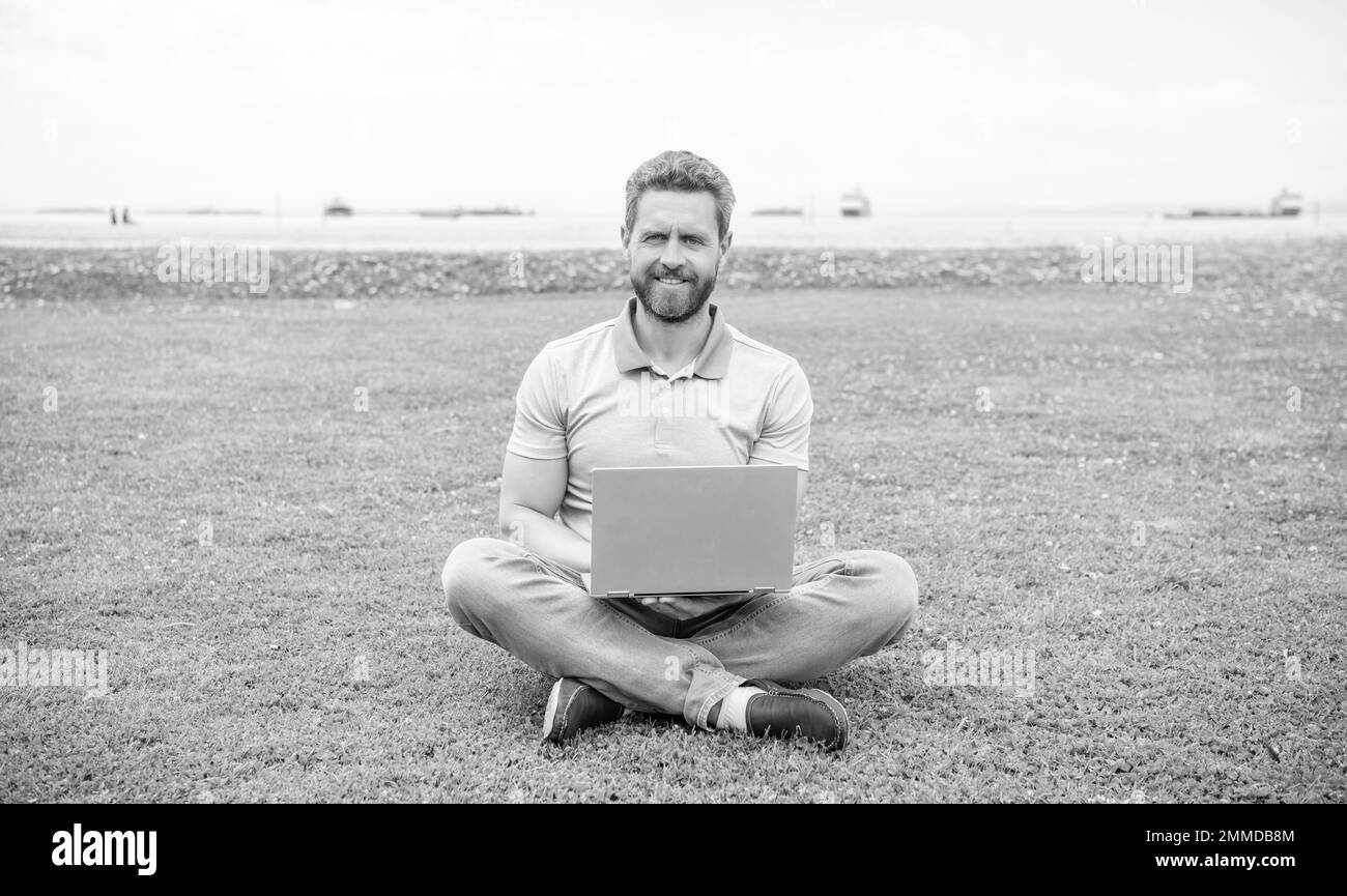 Glücklicher Geschäftsmann mit Laptop zum Bloggen auf grünem Gras, Freiberufler Stockfoto