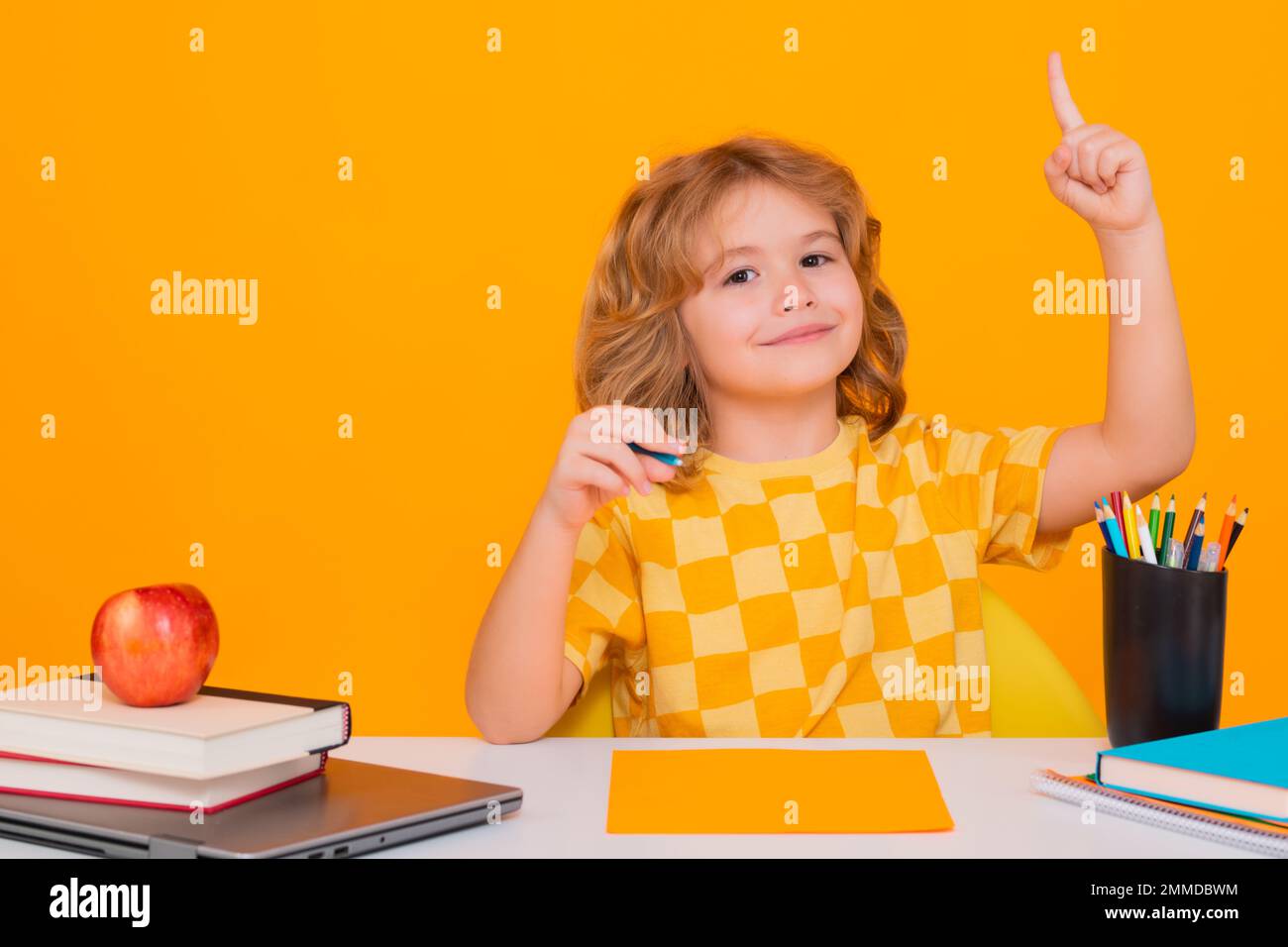 Ein Schulkind, das den Zeigefinger hochhält, mit einer tollen neuen Idee. Schulkinderporträt isoliert auf gelbem Studiohintergrund. Ein Junge aus der Grundschule Stockfoto