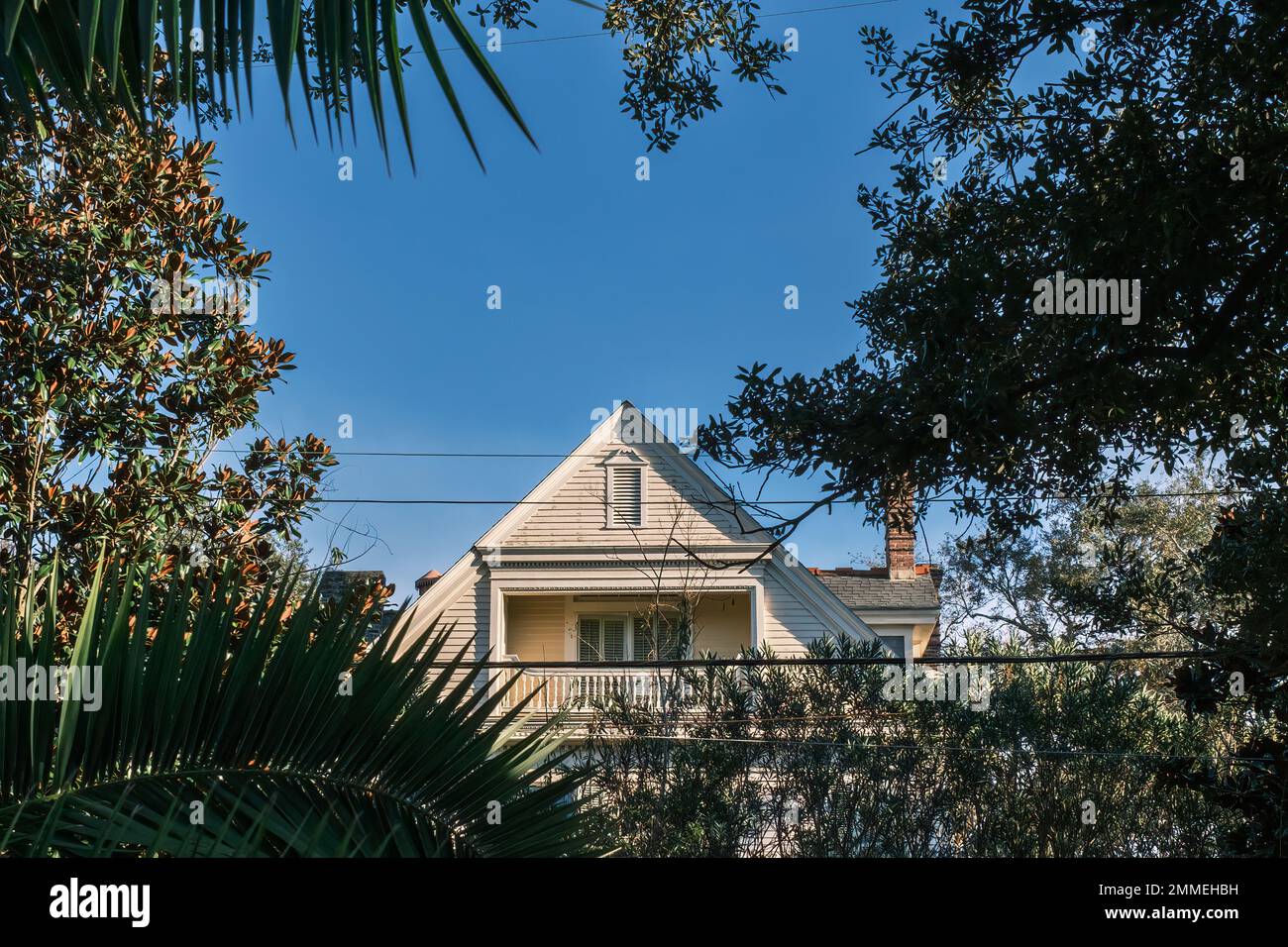 NEW ORLEANS, LA, USA - 27. JANUAR 2023: Versenkter Giebelbalkon im oberen Stockwerk eines historischen Wohnhauses aus der Kolonialzeit, eingerahmt von Baumzweigen Stockfoto