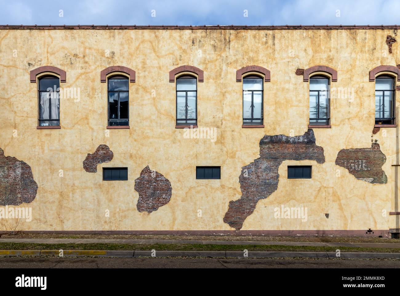 Alte Backsteinwand mit Fenstern und beschädigten Putzstücken in Marshall, Texas Stockfoto