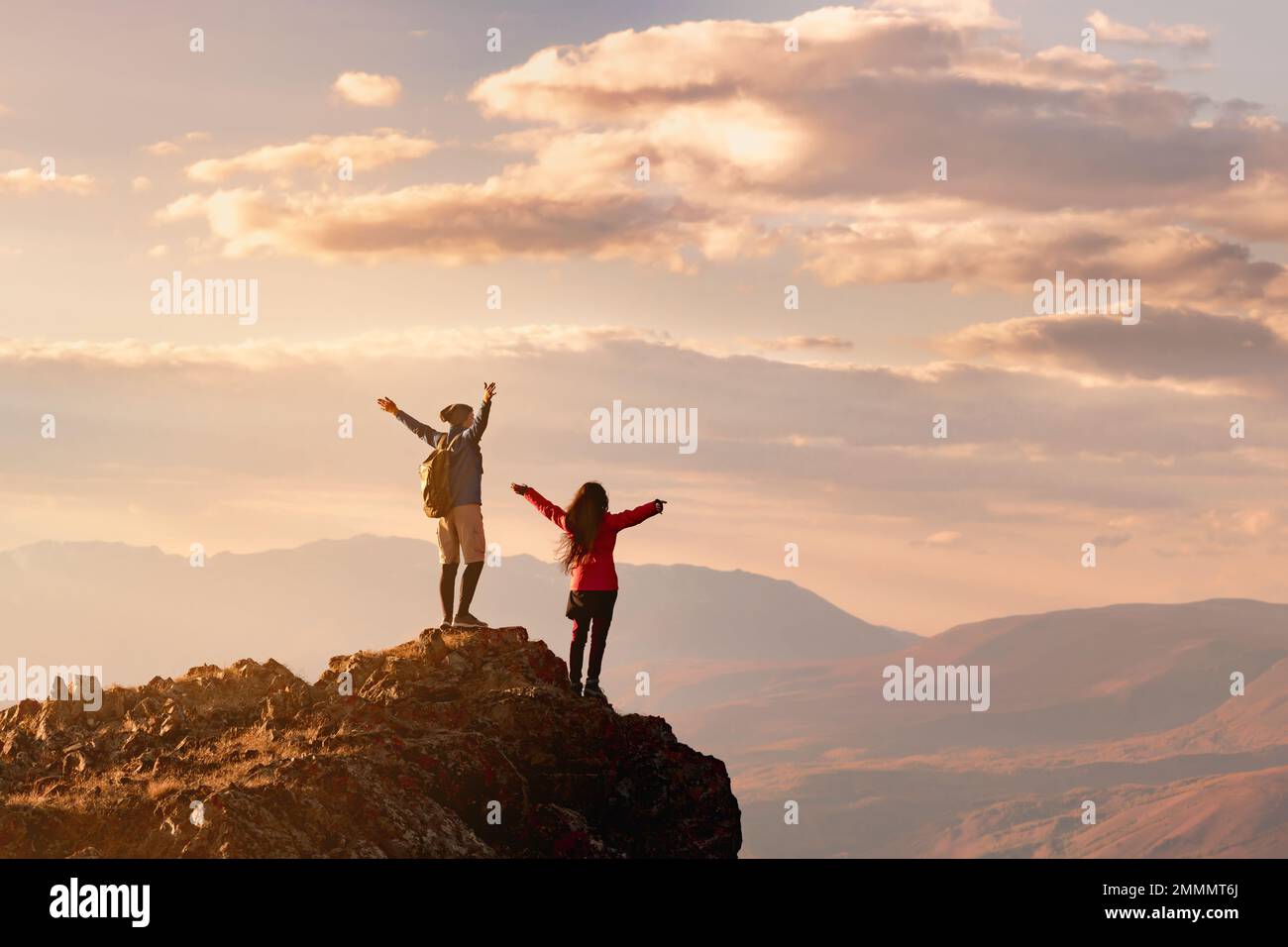 Zwei glückliche Wanderer stehen mit offenen Armen am Aussichtspunkt bei Sonnenuntergang hoch in den Bergen Stockfoto