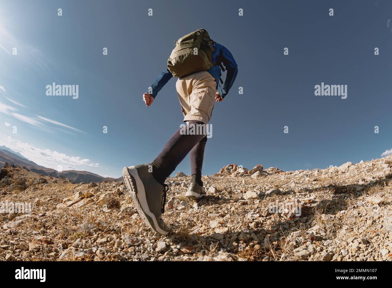 Sportlicher Mann mit Rucksack bergauf in den Bergen. Nahaufnahme von unten Stockfoto
