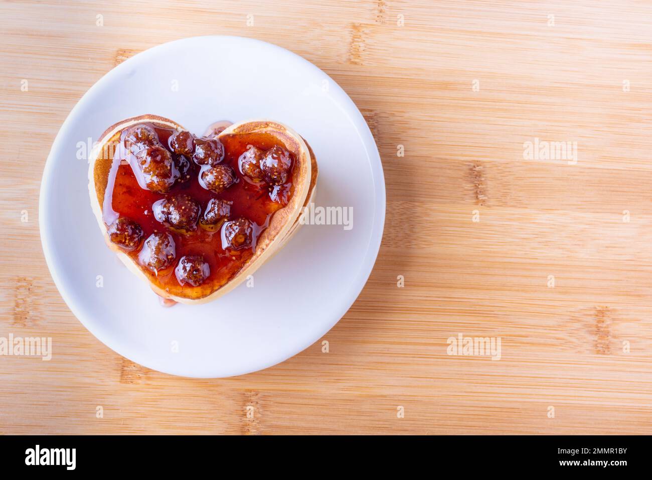 Kreatives Frühstück. Hausgemachte herzförmige Pfannkuchen mit Beerenmarmelade auf weißem Teller auf Holzhintergrund, Kopierbereich, Draufsicht. Postkarte für Valentin Stockfoto