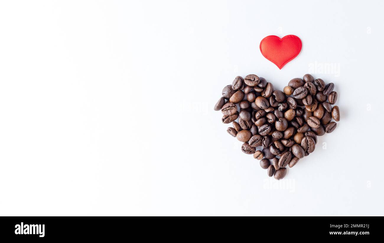 Symbol der Liebe zum Kaffee. Herzform aus Kaffeebohnen und rotem Herz auf weißem Hintergrund, Nahaufnahme, Draufsicht, flach liegend, Kopierbereich, Banner Stockfoto