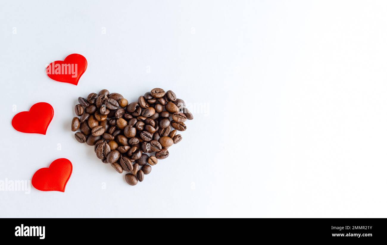 Symbol der Liebe zum Kaffee. Herzform aus Kaffeebohnen und roten Herzen auf weißem Hintergrund, Nahaufnahme, Draufsicht, flach liegend, Kopierbereich, Banner Stockfoto