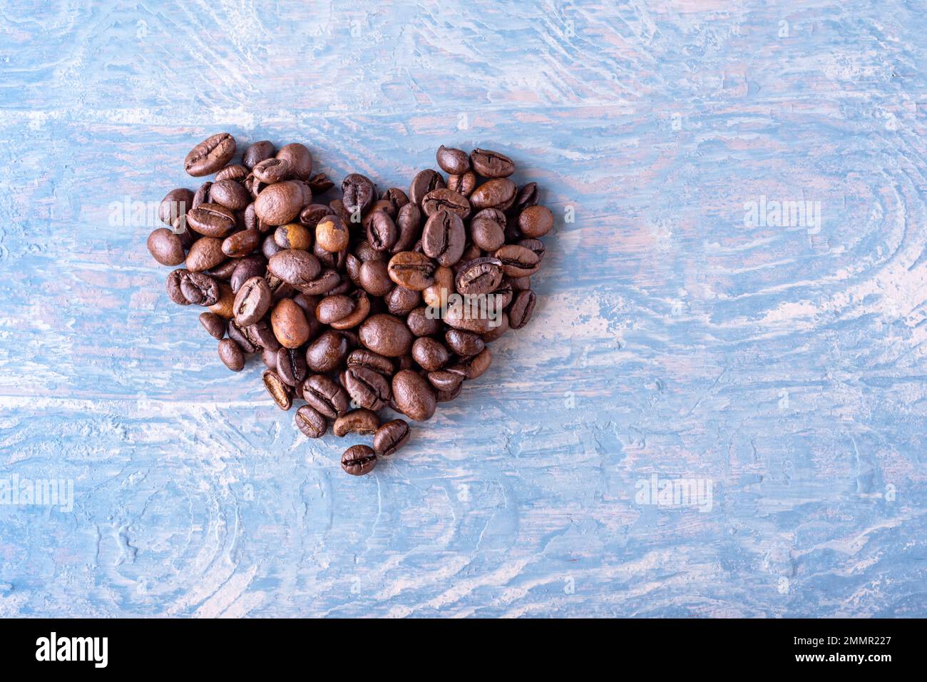 Herzform aus Kaffeebohnen auf blauem, stilvollem Holzhintergrund, Nahaufnahme, Draufsicht, flach liegend. Symbol der Liebe zum Kaffee. Stockfoto