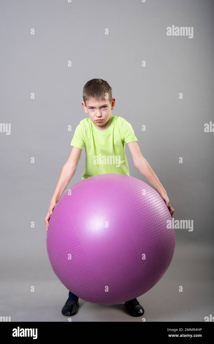 Porträt eines süßen, verärgerten Jungen, der sich nicht mit fit Ball befassen will. Das Konzept, nicht Sport treiben zu wollen, körperliche Schwäche Stockfoto