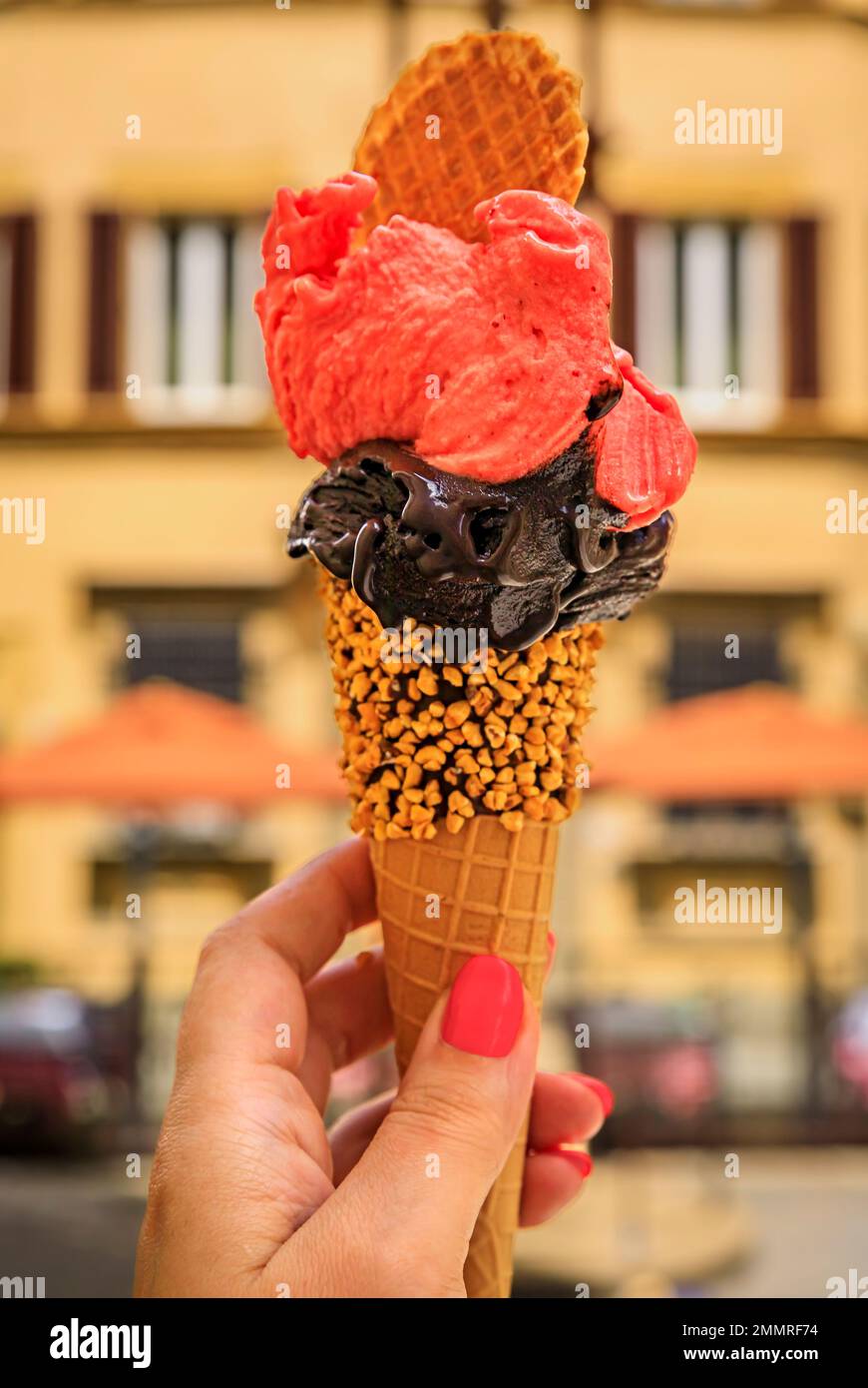 Halten Sie ein handgemachtes Schokoladen- und Himbeergelato in der Hand, und genießen Sie den Blick auf verschwommene Häuser und Lichter auf einer Fußgängerstraße im Centro Storico, Florenz, Italien Stockfoto