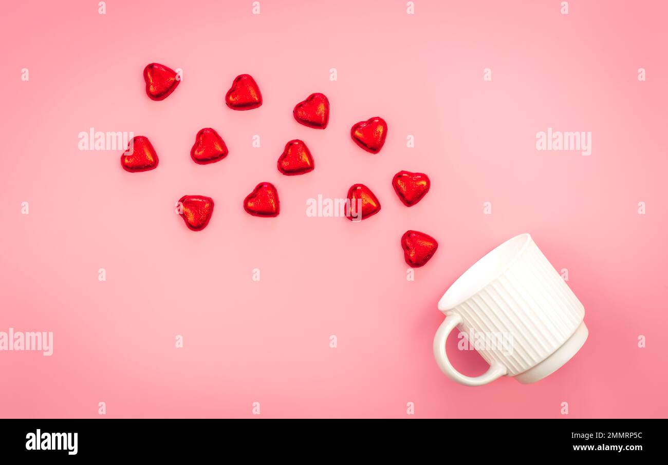 Eine Tasse und verstreute herzförmige Süßigkeiten auf pinkfarbenem Hintergrund, flach liegend. Stockfoto