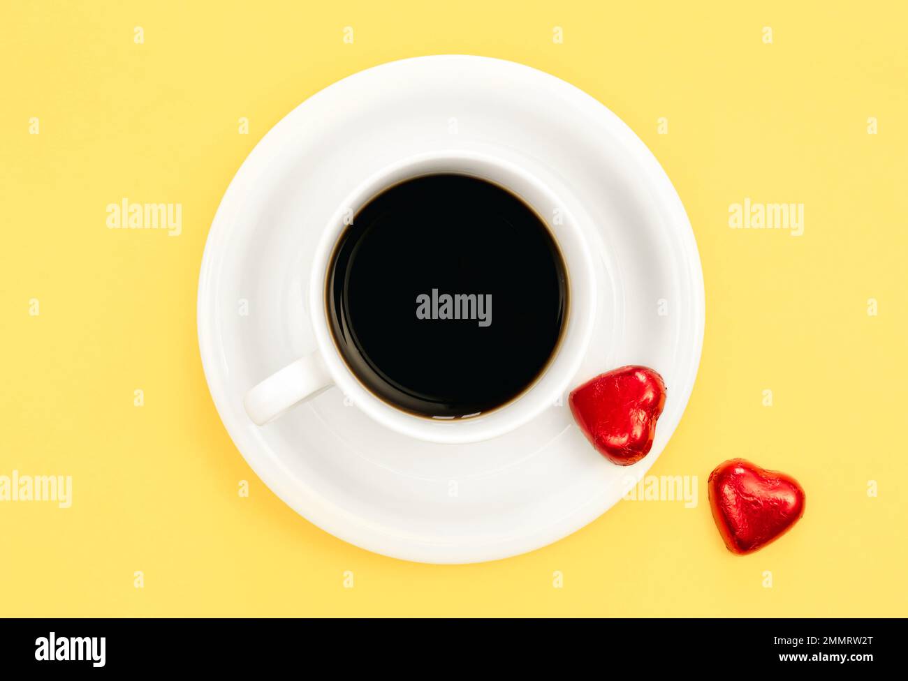 Eine Tasse Kaffee und herzförmige Süßigkeiten auf gelbem Hintergrund, flach liegend. Stockfoto