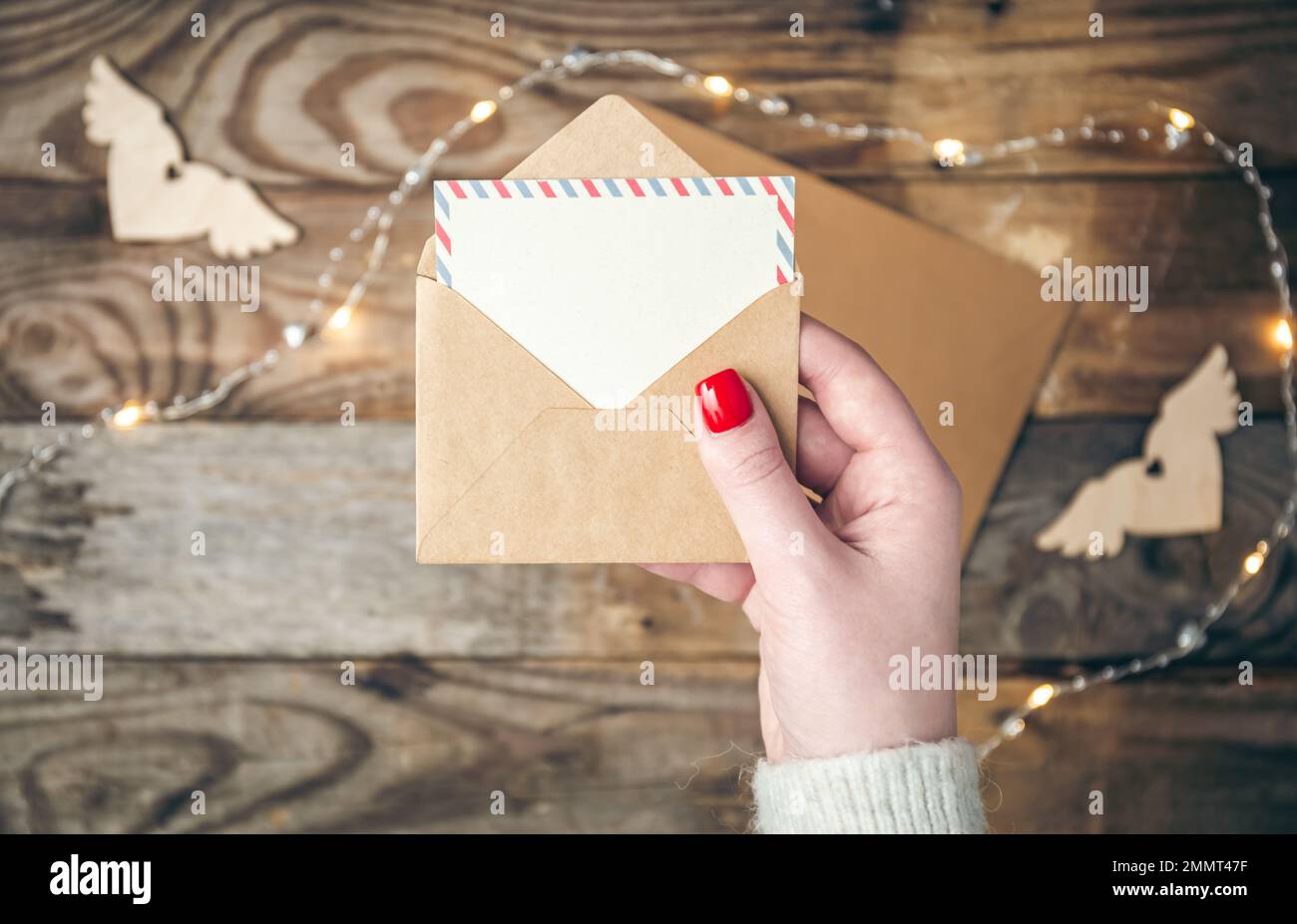 Leere Postkarte und Umschlag in weiblichen Händen auf unscharfem Holzhintergrund. Stockfoto