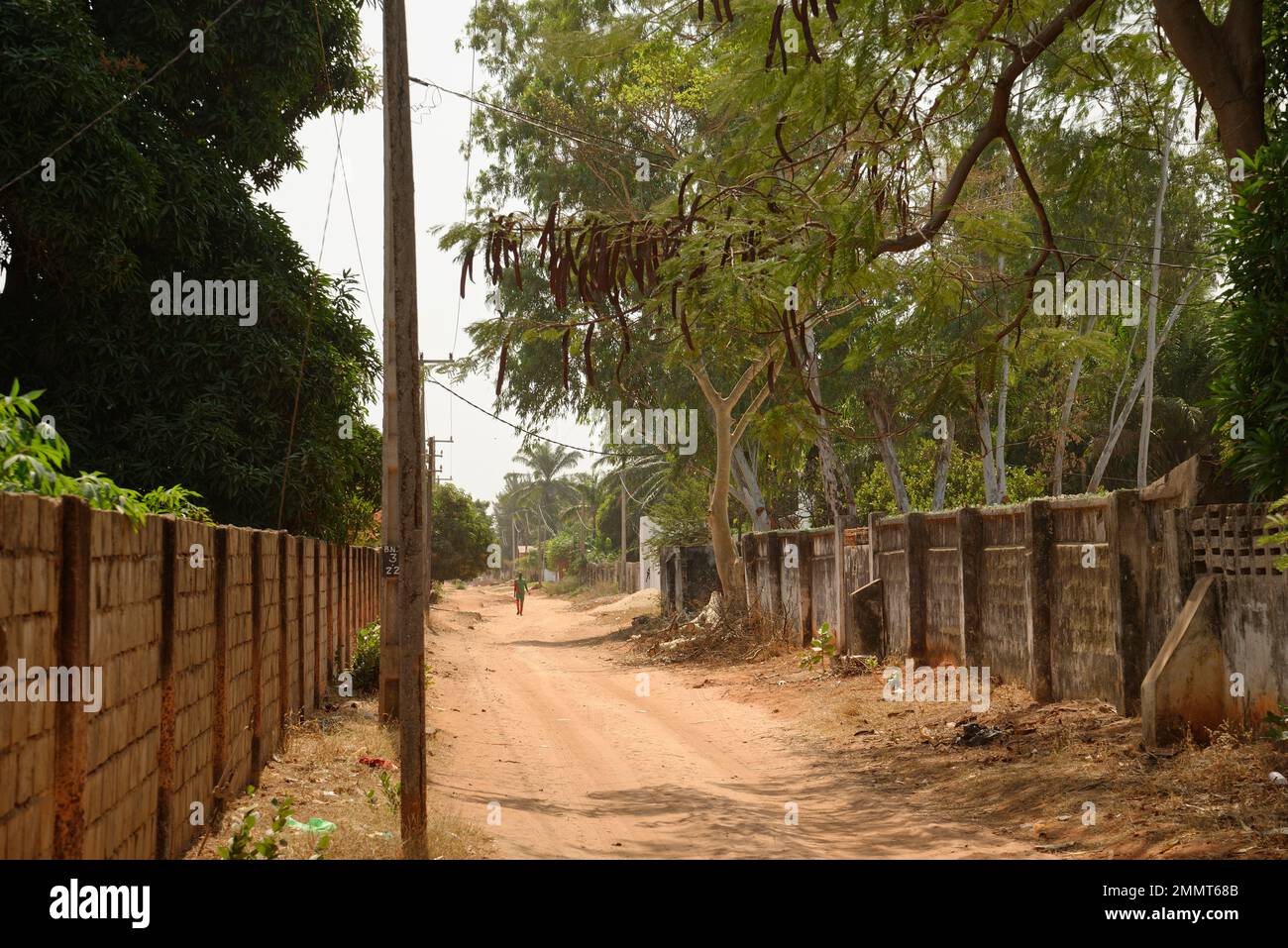 Straßenszene in Gambia, Westafrika. Ein subtropisches, warmes und sonniges Winterziel für Nordeuropäer. Ein Mann, der die Straße entlang läuft. Stockfoto