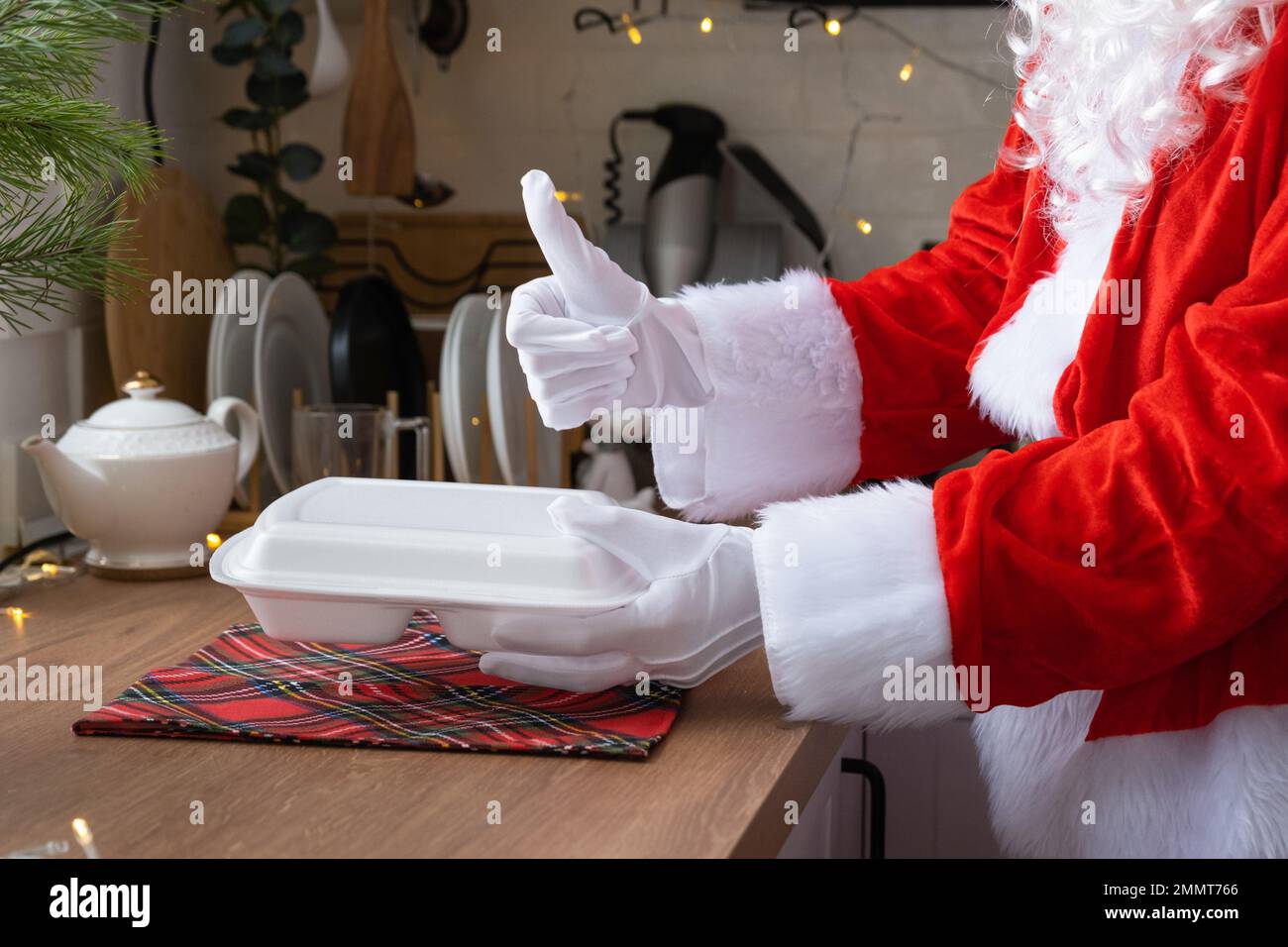 Die Lieferung von Lebensmitteln an den Heim-Service-Container in den Händen des Weihnachtsmanns legt sie auf den Küchentisch und nimmt sie mit, Daumen hoch. Eine scharfe Bestellung, Christma Stockfoto