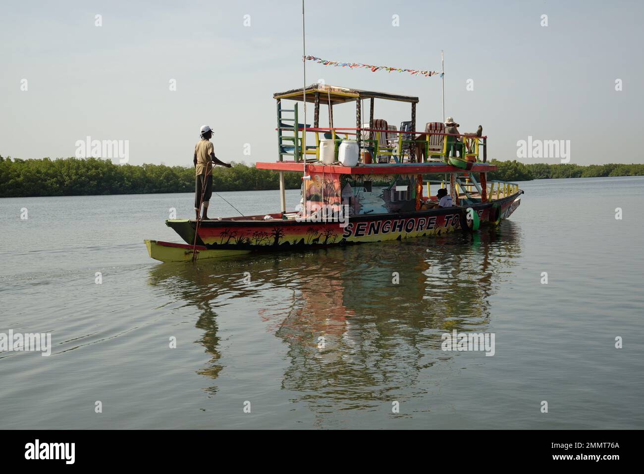 Ein Touristenboot auf einem Nebenfluss des Gambia. Zwei Angestellte und ein einziger Tourist mit Kamera. Ein langes Objektiv zum Fotografieren von Wildtieren, insbesondere Vögeln. Stockfoto