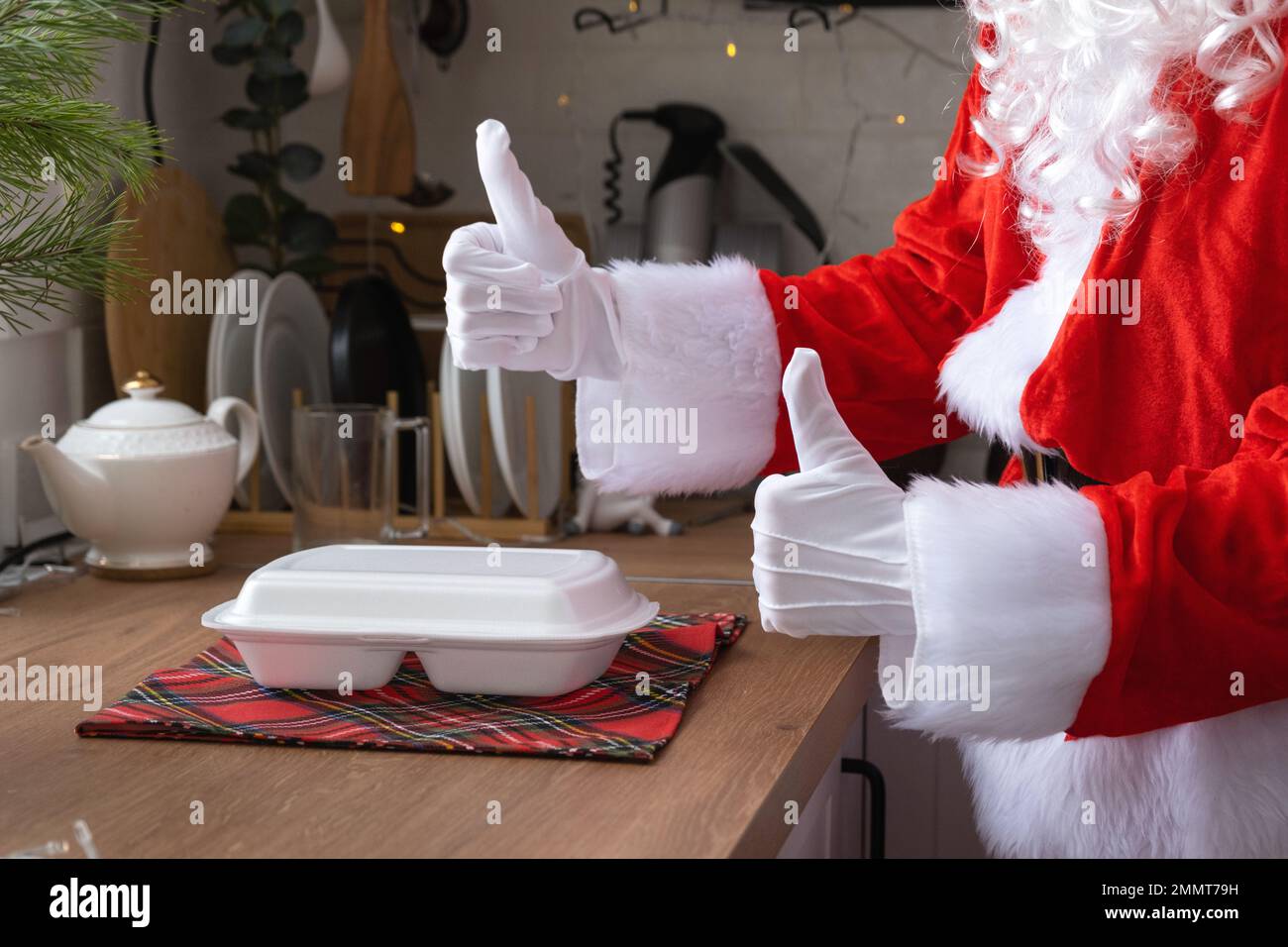 Die Lieferung von Lebensmitteln an den Heim-Service-Container in den Händen des Weihnachtsmanns legt sie auf den Küchentisch und nimmt sie mit, Daumen hoch. Eine scharfe Bestellung, Christma Stockfoto
