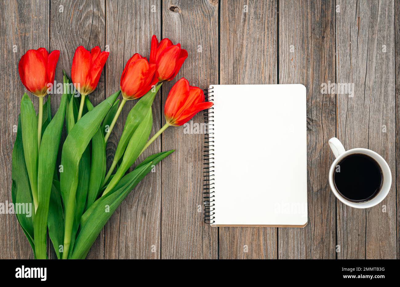 Strauß roter Tulpen, Tasse Kaffee und Notizbuch auf Holzhintergrund. Stockfoto