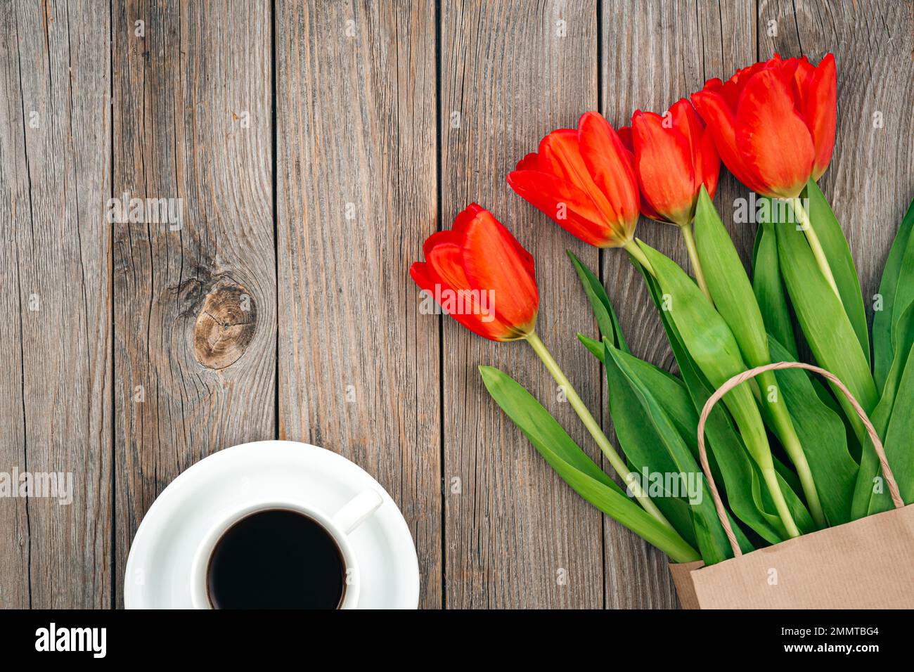 Strauß roter Tulpen und eine Tasse Kaffee auf Holzhintergrund, Draufsicht. Stockfoto