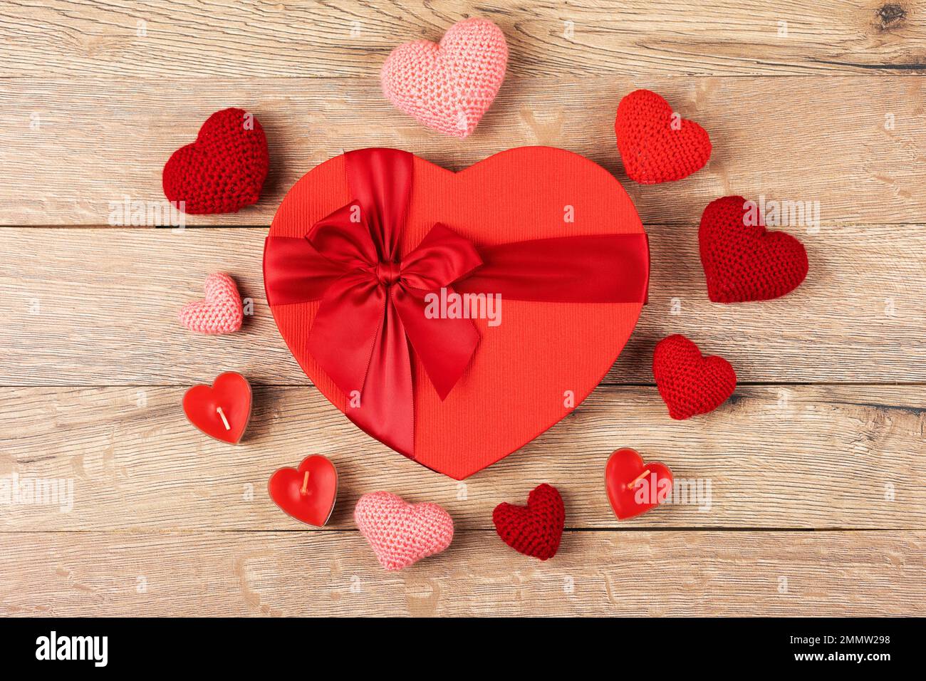 Rote Geschenkbox mit gestrickten roten und rosa Herzen und mit roten Kerzen in Herzform auf Holzhintergrund. Alles gute zum Valentinstag, Mutter Papa Stockfoto