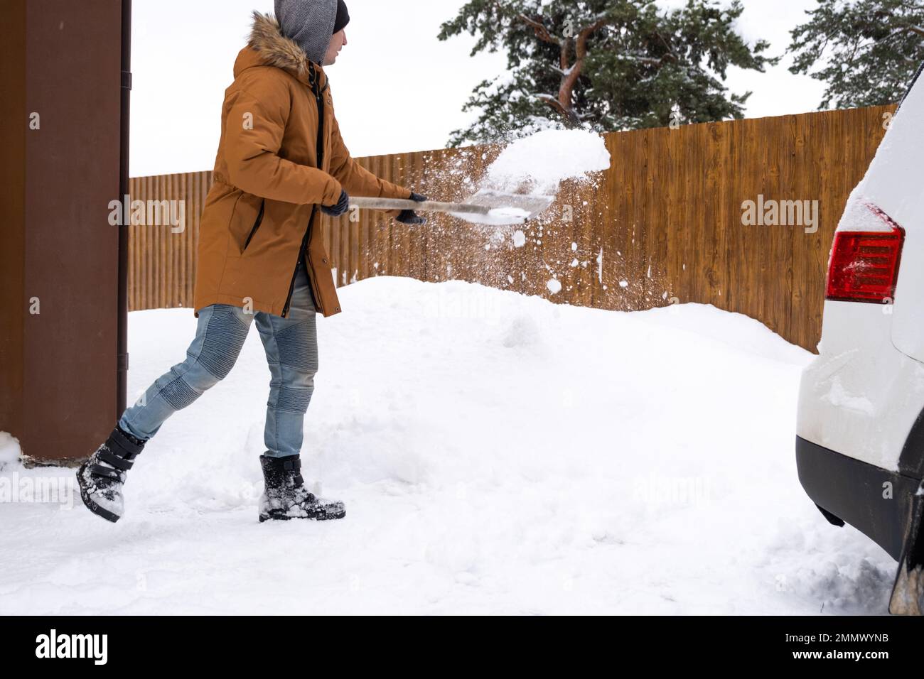 Ein Mann im Winter reinigt Schnee mit einer Schaufel im Hof eines Hauses auf dem Parkplatz. Schneefall, schwierige Wetterbedingungen, das Auto steht still, digg Stockfoto