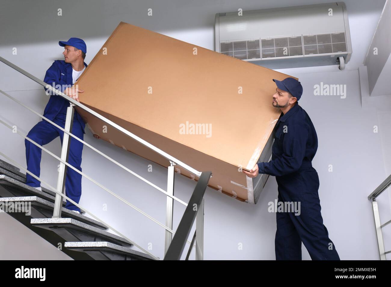 Professionelle Arbeiter, die Kühlschränke auf Treppen in Gebäuden tragen Stockfoto