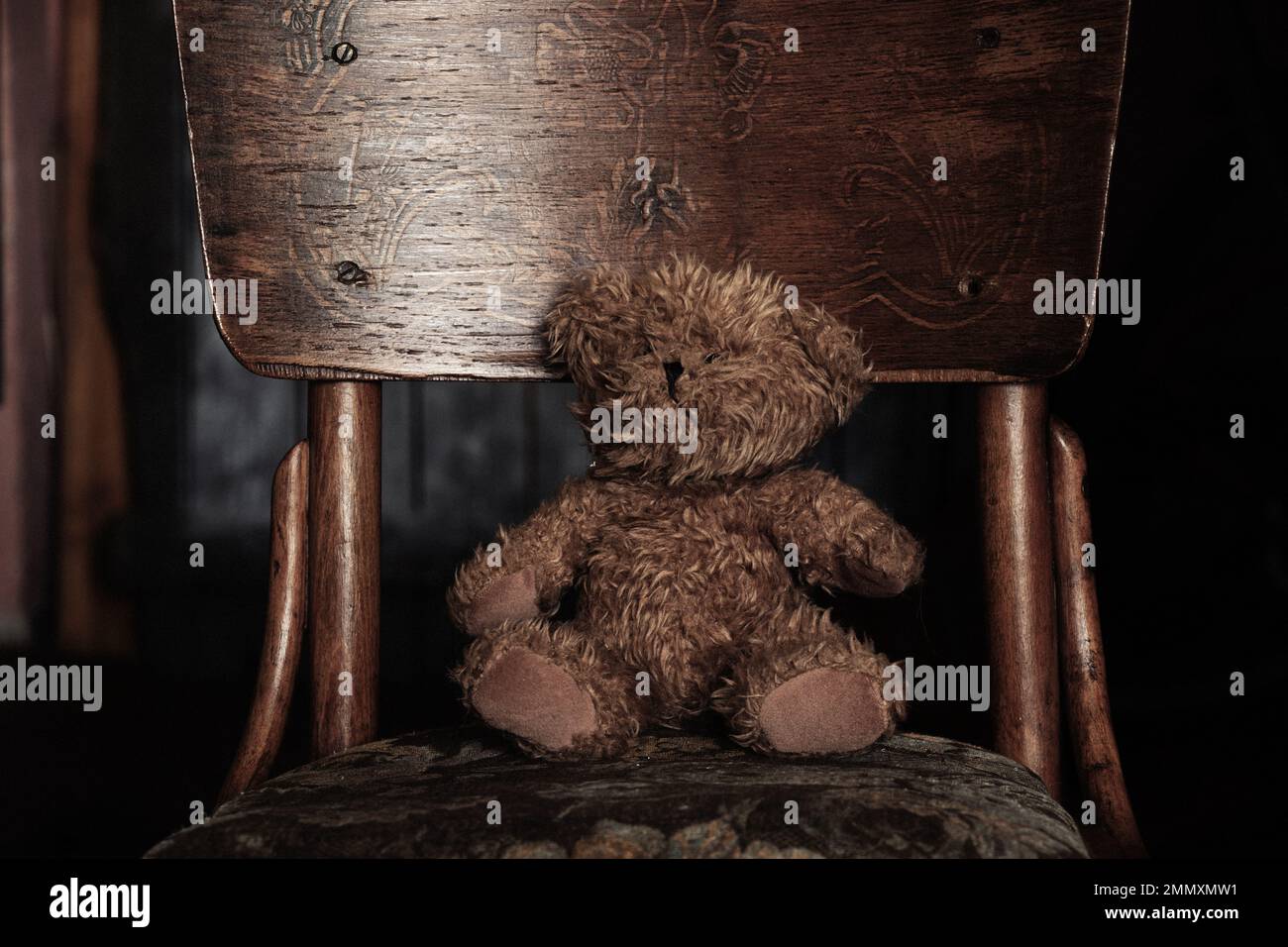 teddybär sitzt auf einem alten weichen Stuhl im Dunkeln im Zimmer zu Hause, Kinderspielzeug, Teddybär Stockfoto