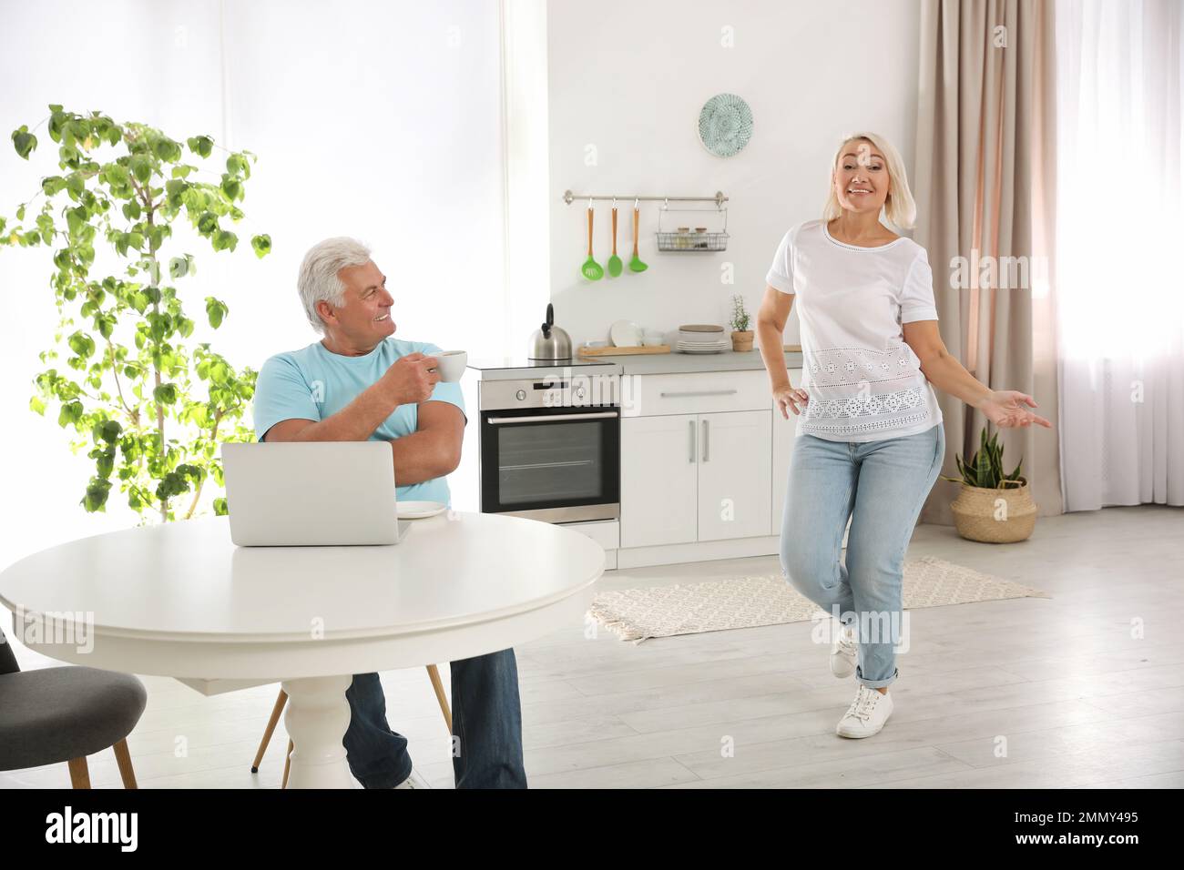 Eine Frau mittleren Alters, die neben ihrem Mann in der Küche tanzt. Glückliches reifes Paar Stockfoto