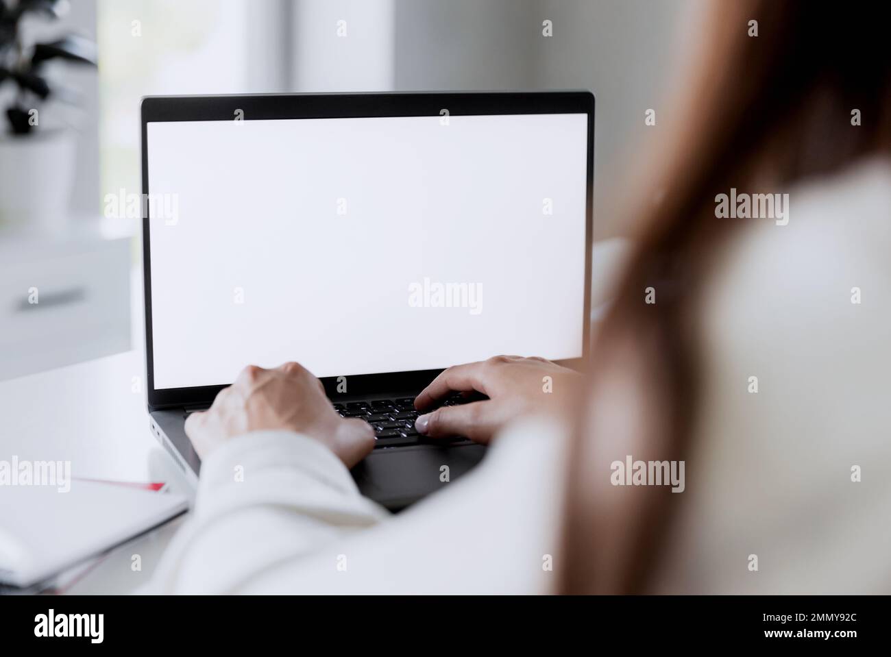 Weibliche Hände tippen auf dem Laptop mit leerem weißen Bildschirmmodell. Der Computer liegt auf dem weißen Tisch. Unscharfer Hintergrund. Person, die von zu Hause aus arbeitet Concept. Bereichsbereich für Text kopieren Stockfoto